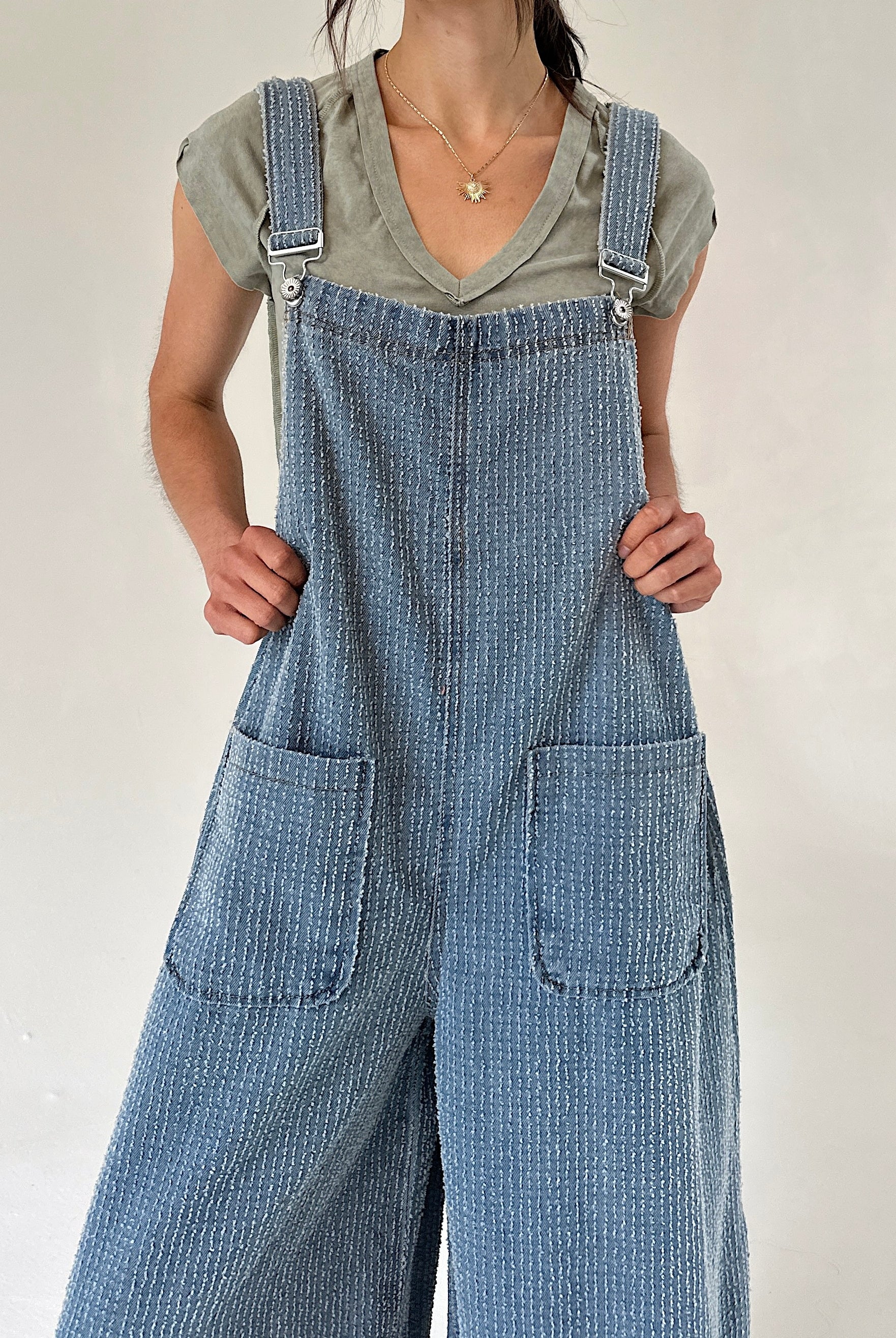 Person wearing blue denim textured overalls over a green t-shirt against a plain background