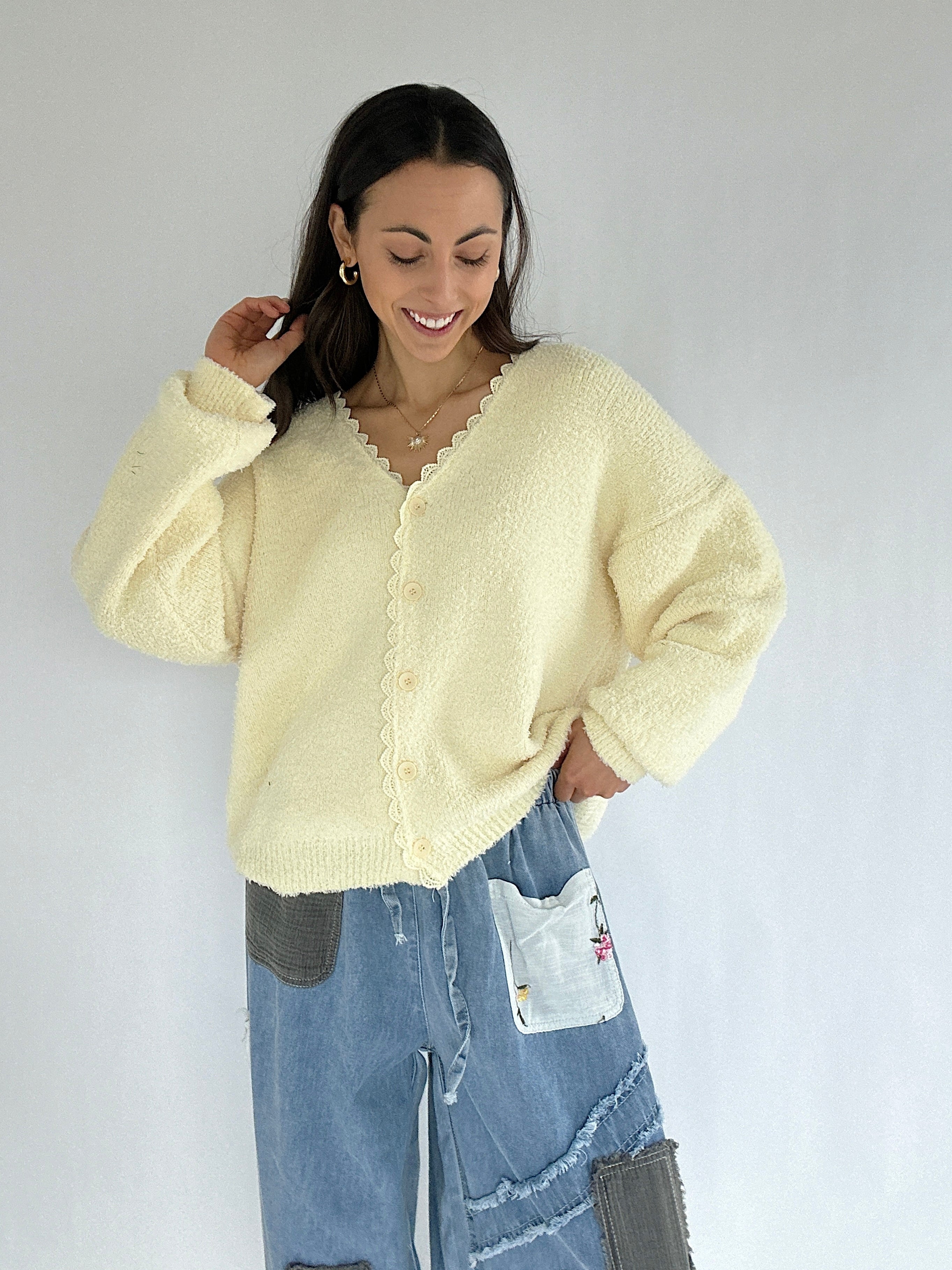 Woman wearing a light yellow cardigan over a white top with blue jeans against a plain background