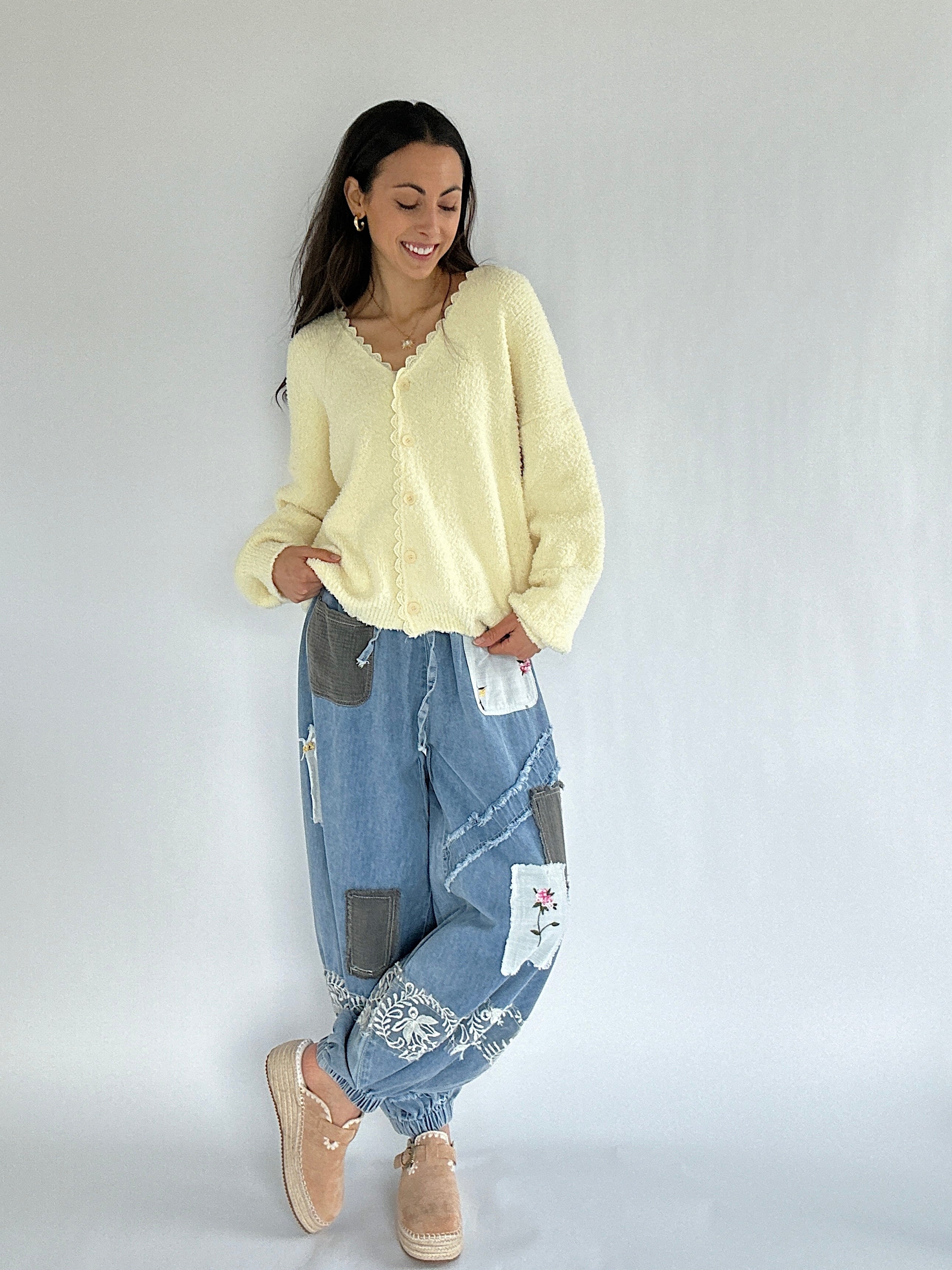 Woman wearing a light yellow cardigan and blue patchwork jeans on a white background