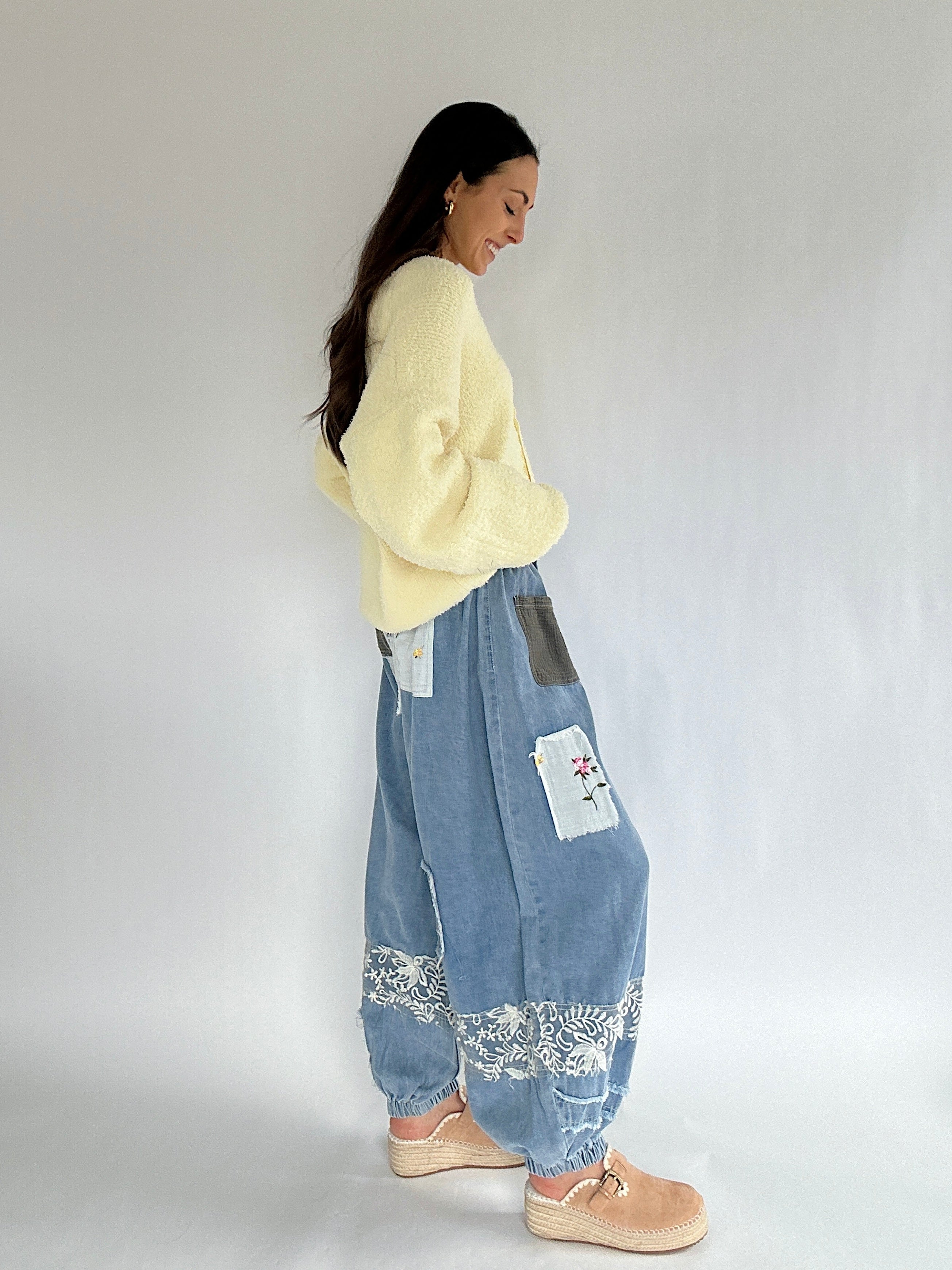 Woman wearing a yellow sweater and blue patchwork pants on a plain background showing the side profile