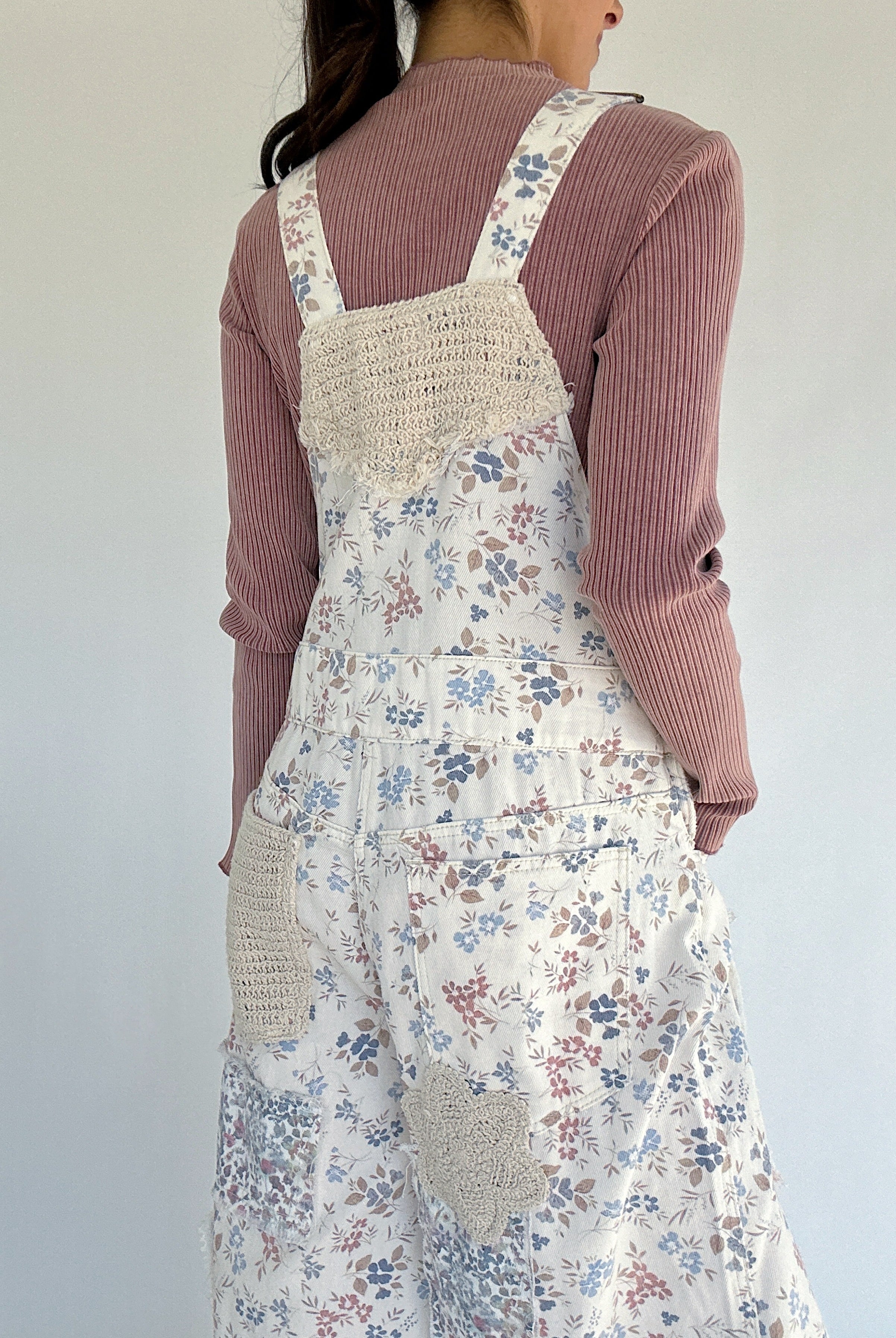 Person wearing floral overalls over a pink sweater against a white background