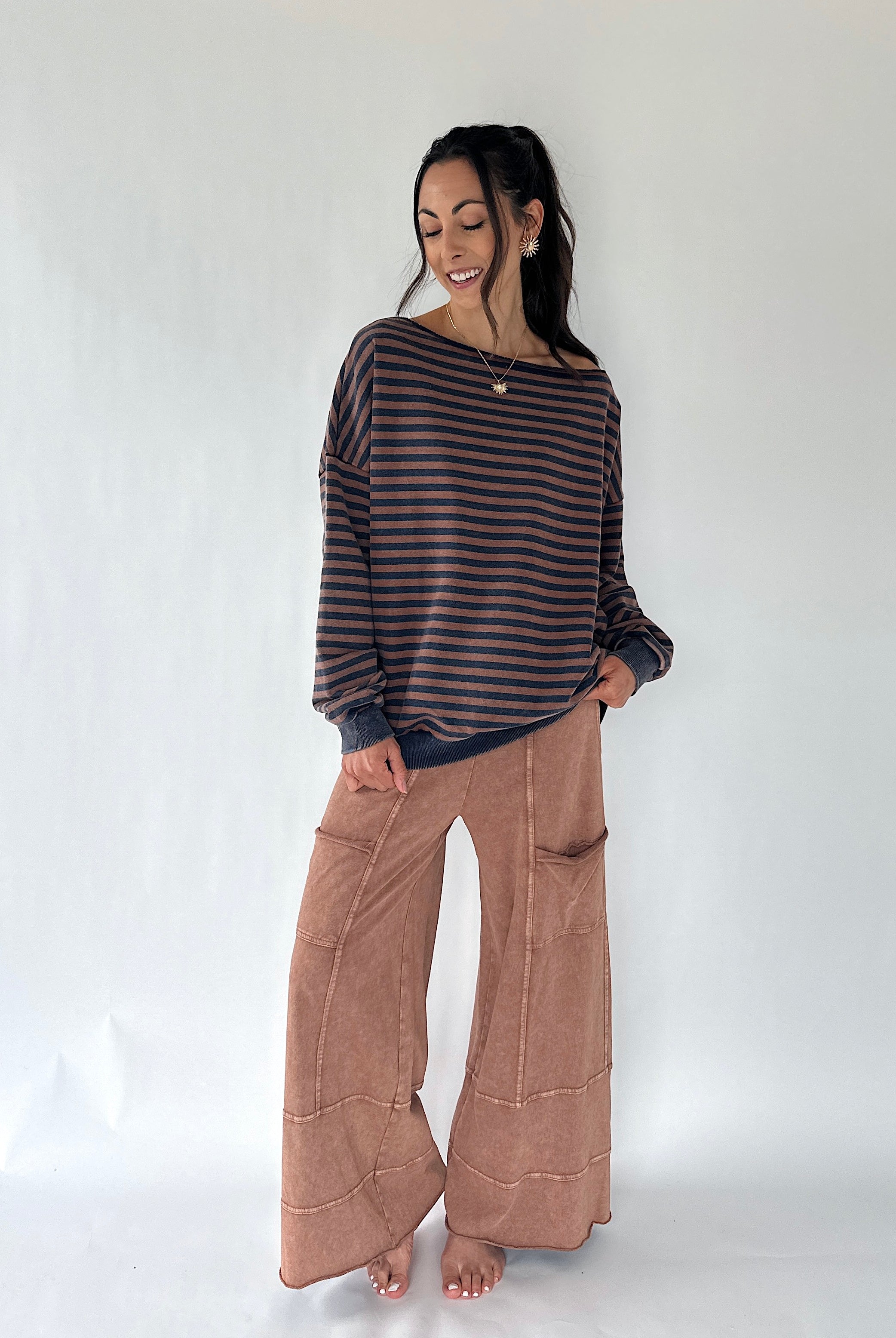 A woman modeling a dark brown and black striped long-sleeve knit top with wide-leg brown pants, standing against a plain white studio background.