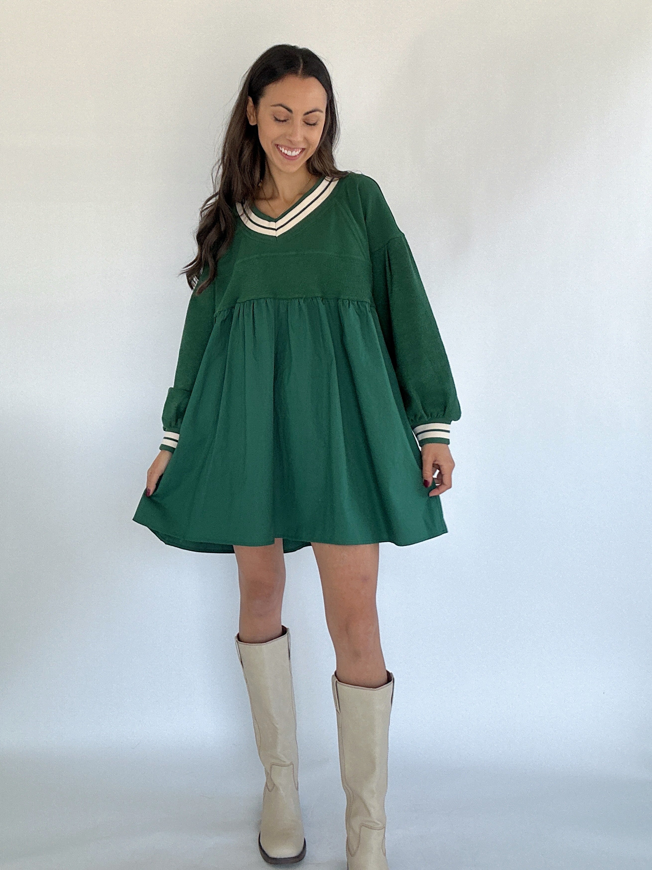 Woman wearing a green dress with white trim and beige knee-high boots against a white background