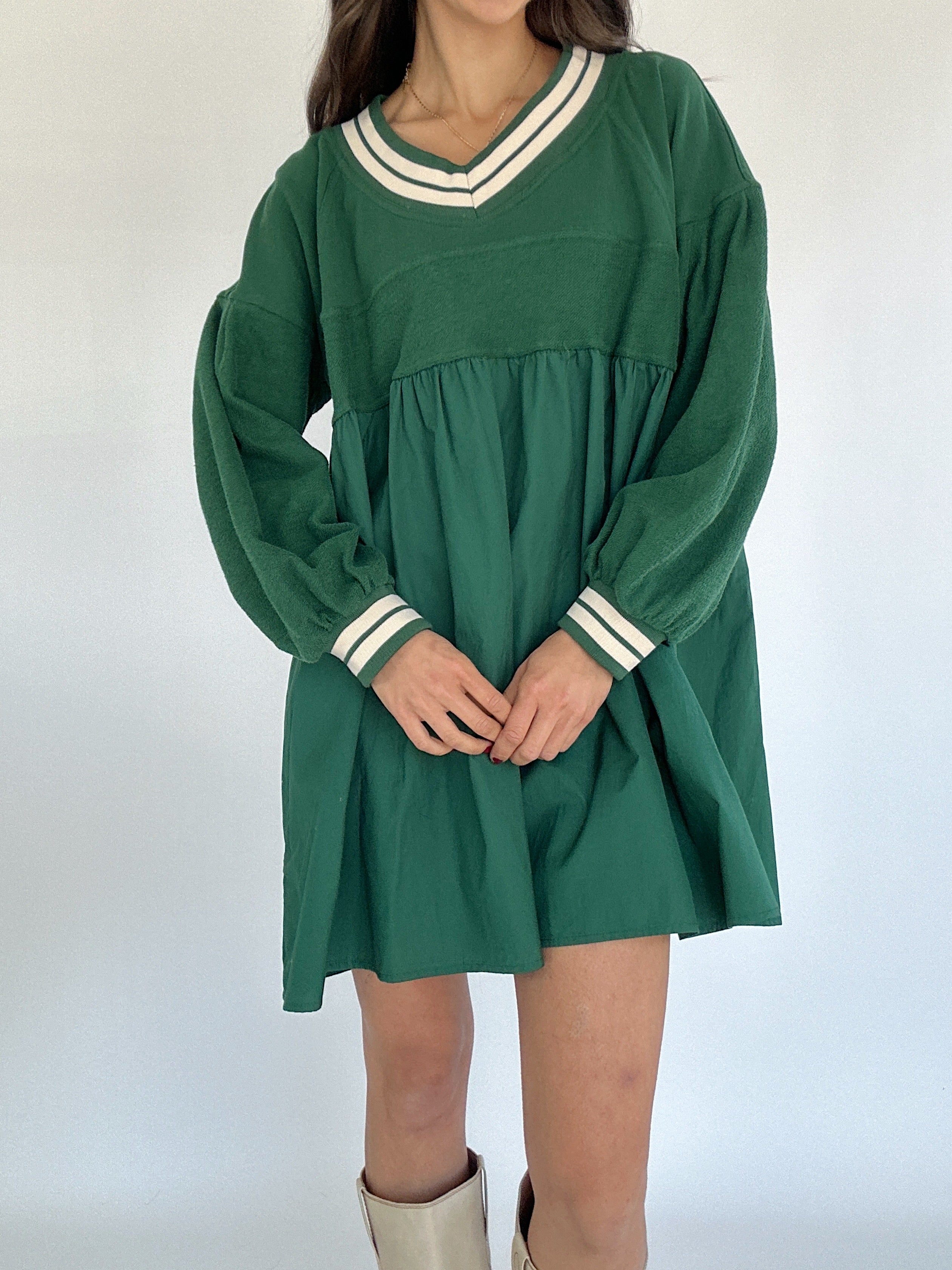 Green dress with long sleeves and white trim worn by a person on a plain background
