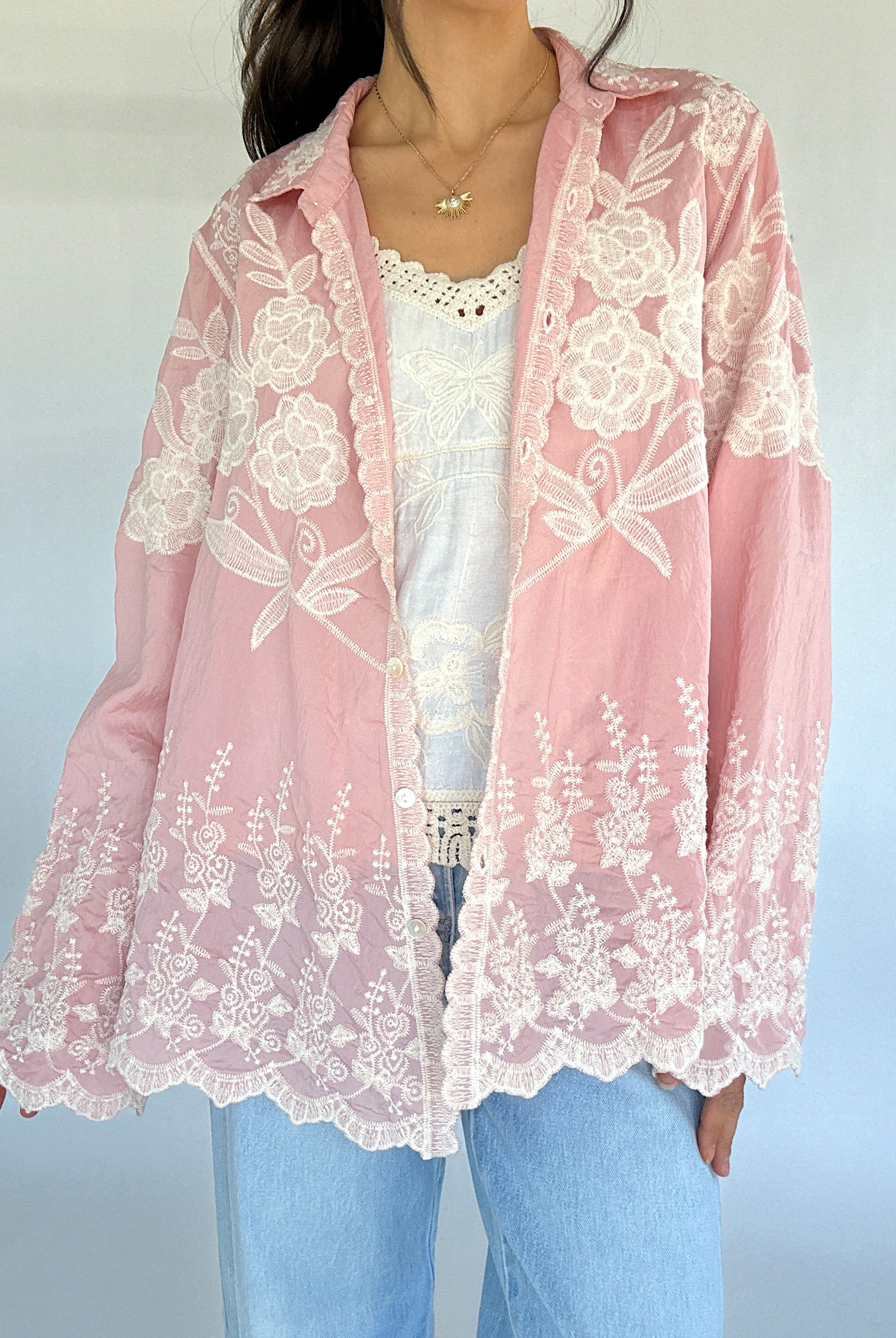 Pink lace cardigan over a white top and blue jeans on a light gray background
