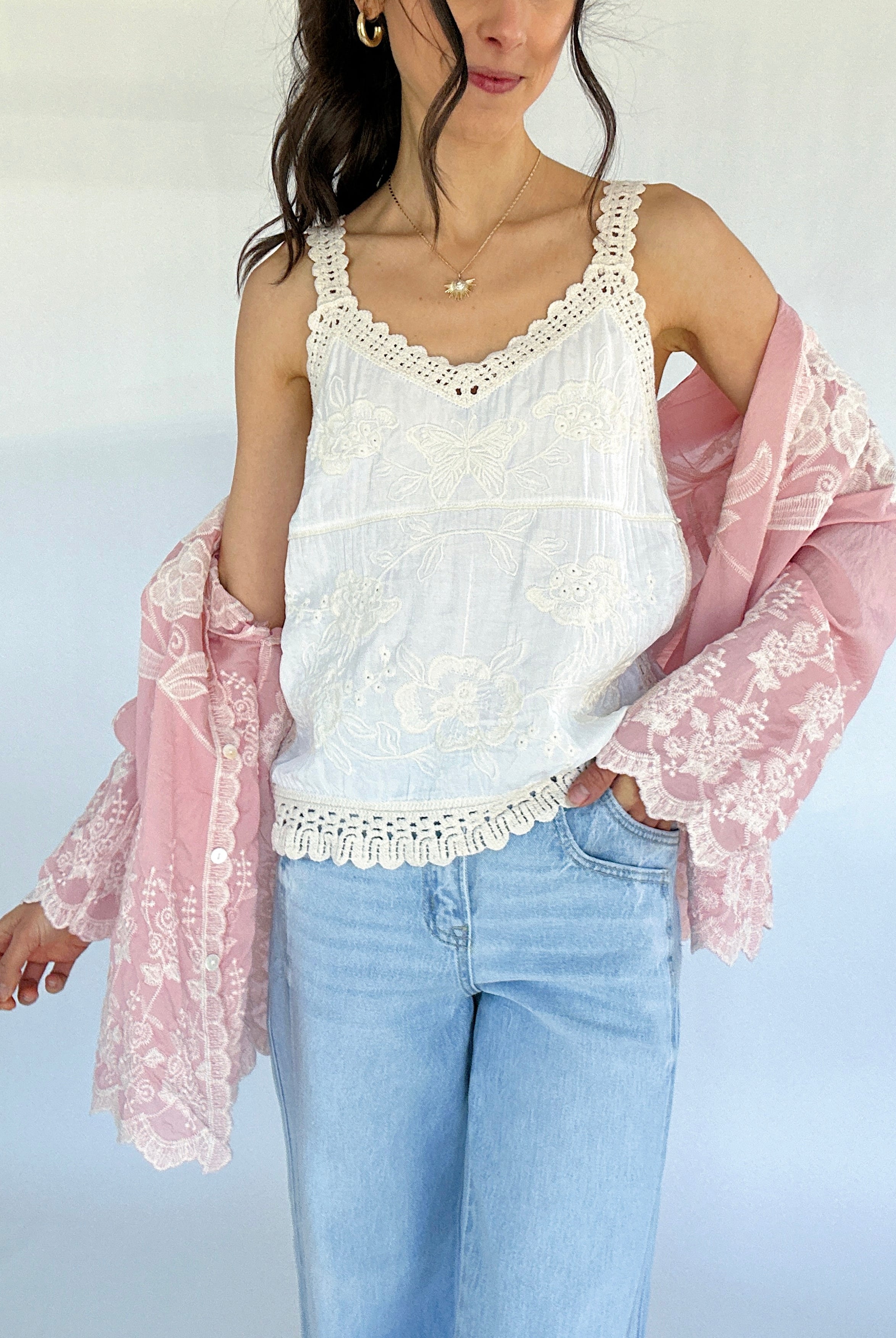 Woman wearing a white lace top with a pink sheer cardigan against a light background