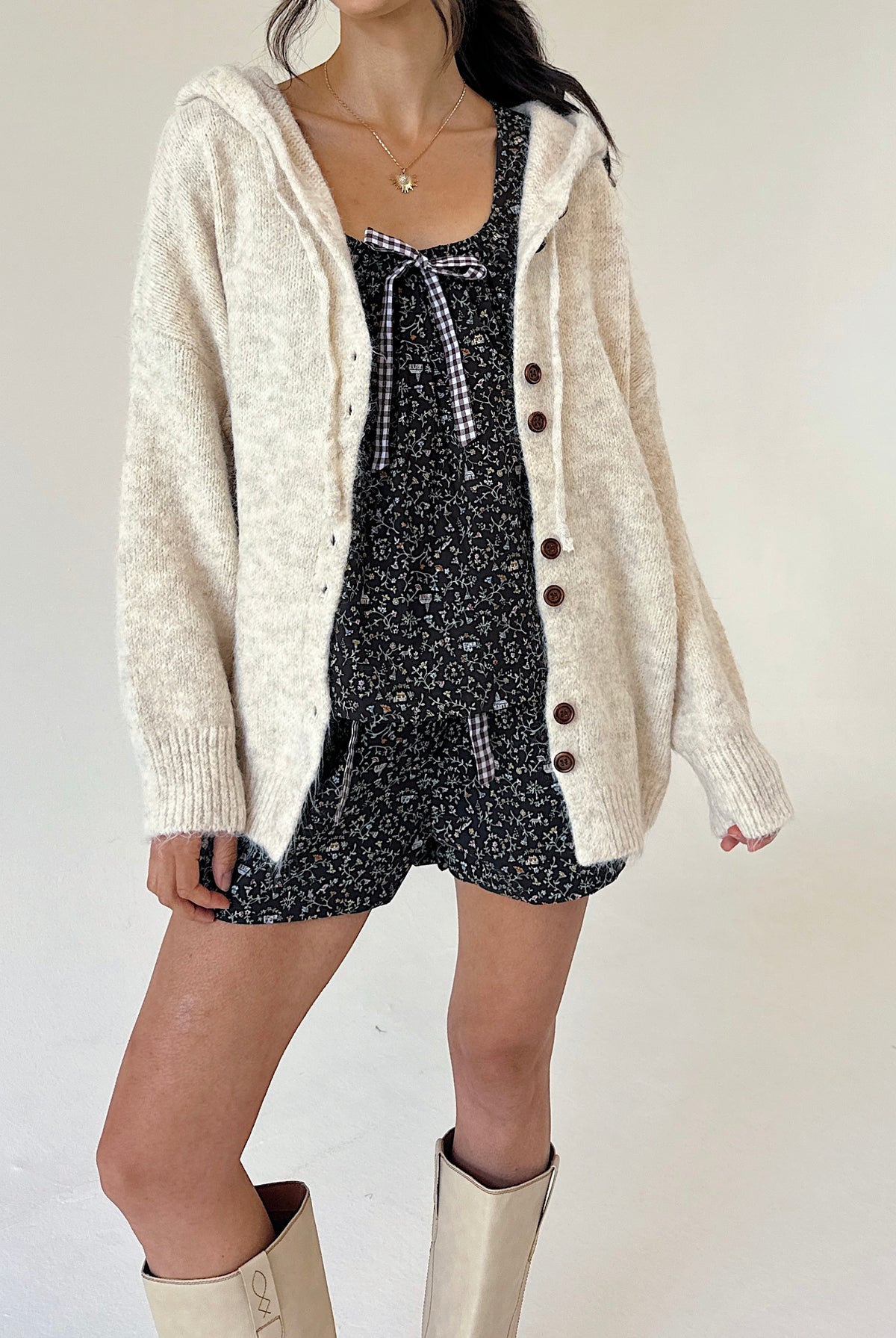 A model wearing a cream-colored, fuzzy knit cardigan over a floral tank and short set, paired with cream-colored knee-high boots, against a plain off-white background.