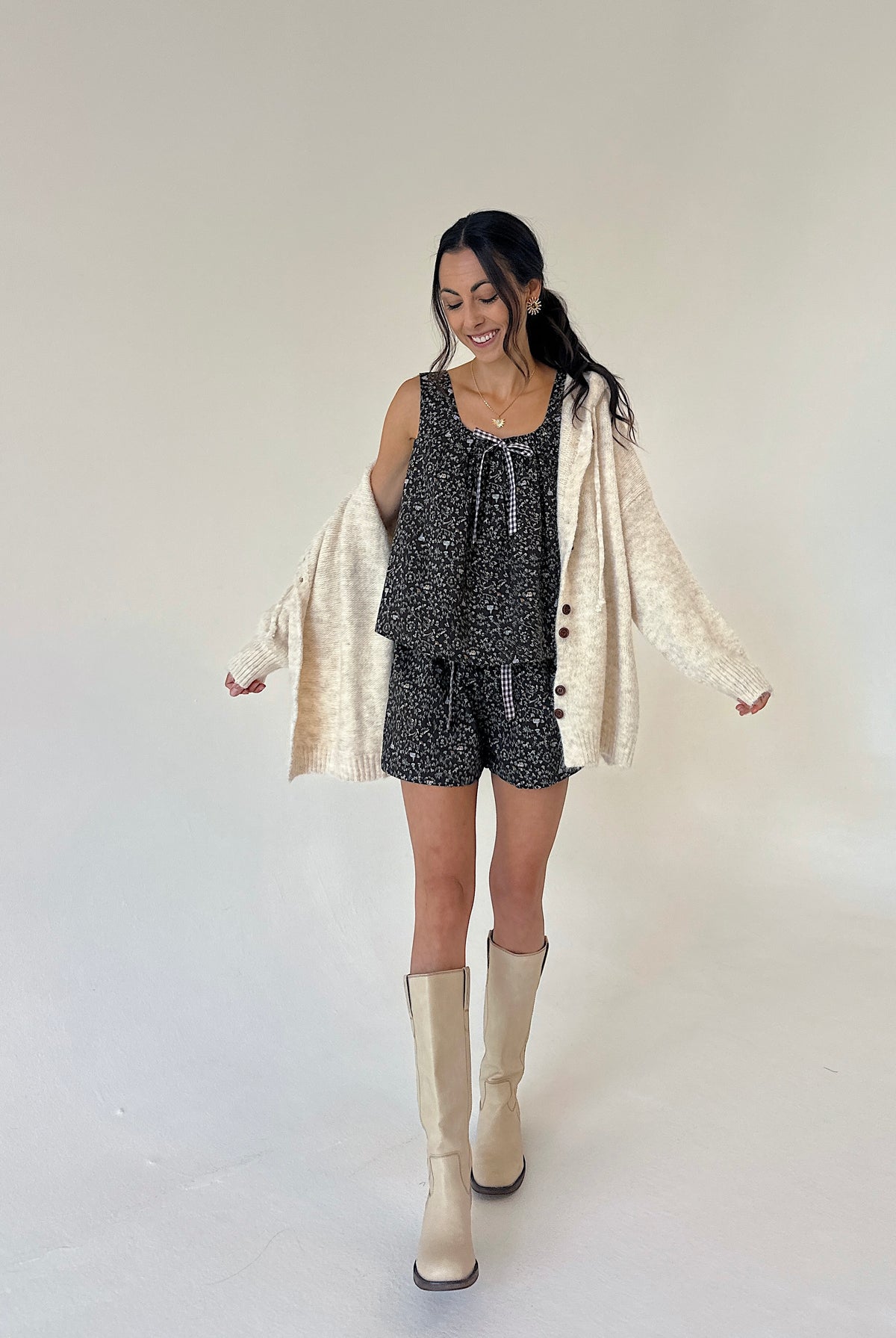 A woman modeling a matching two-piece lounge set with a black and white speckled pattern, styled with a cream-colored cardigan and cream-colored knee-high boots against a plain studio background.