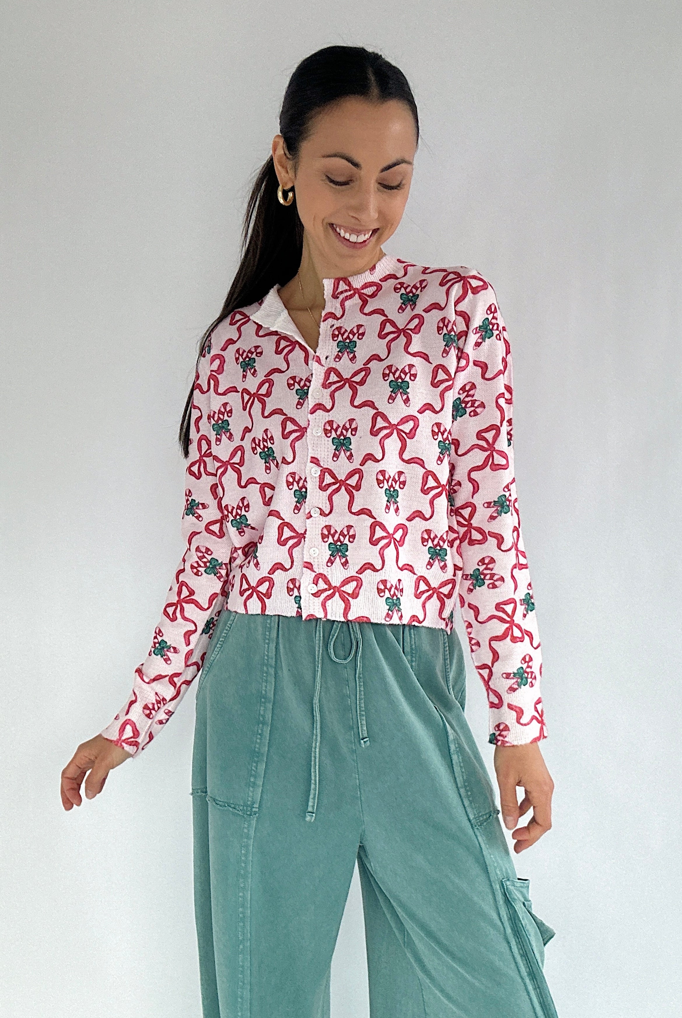 Woman wearing a candy cane and bow printed cardigan and teal pants on a white background
