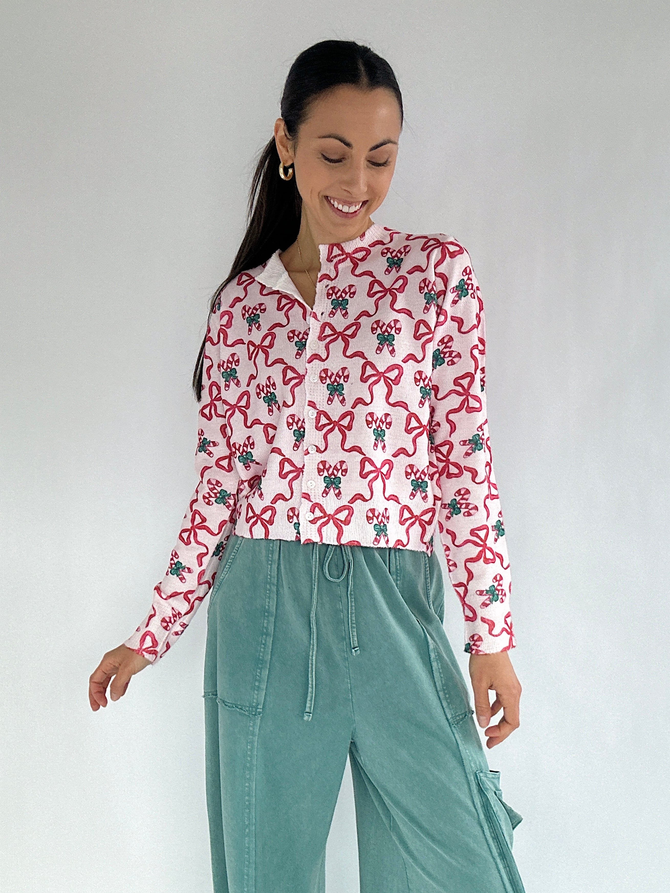 Woman wearing a candy cane and bow printed cardigan and teal pants on a white background
