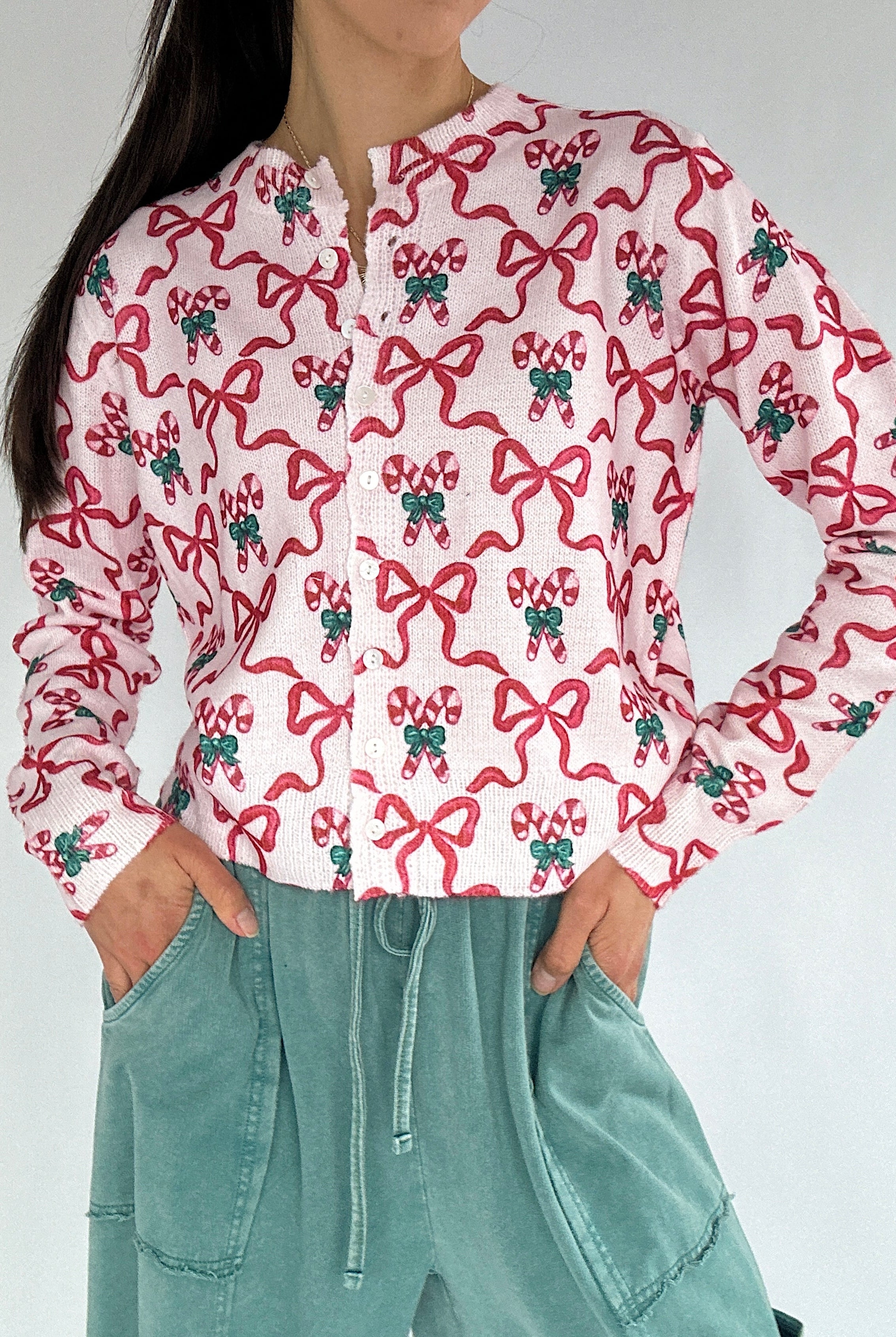 Person wearing a white shirt with red bow and candy cane pattern and green accents, paired with teal pants on a plain background.