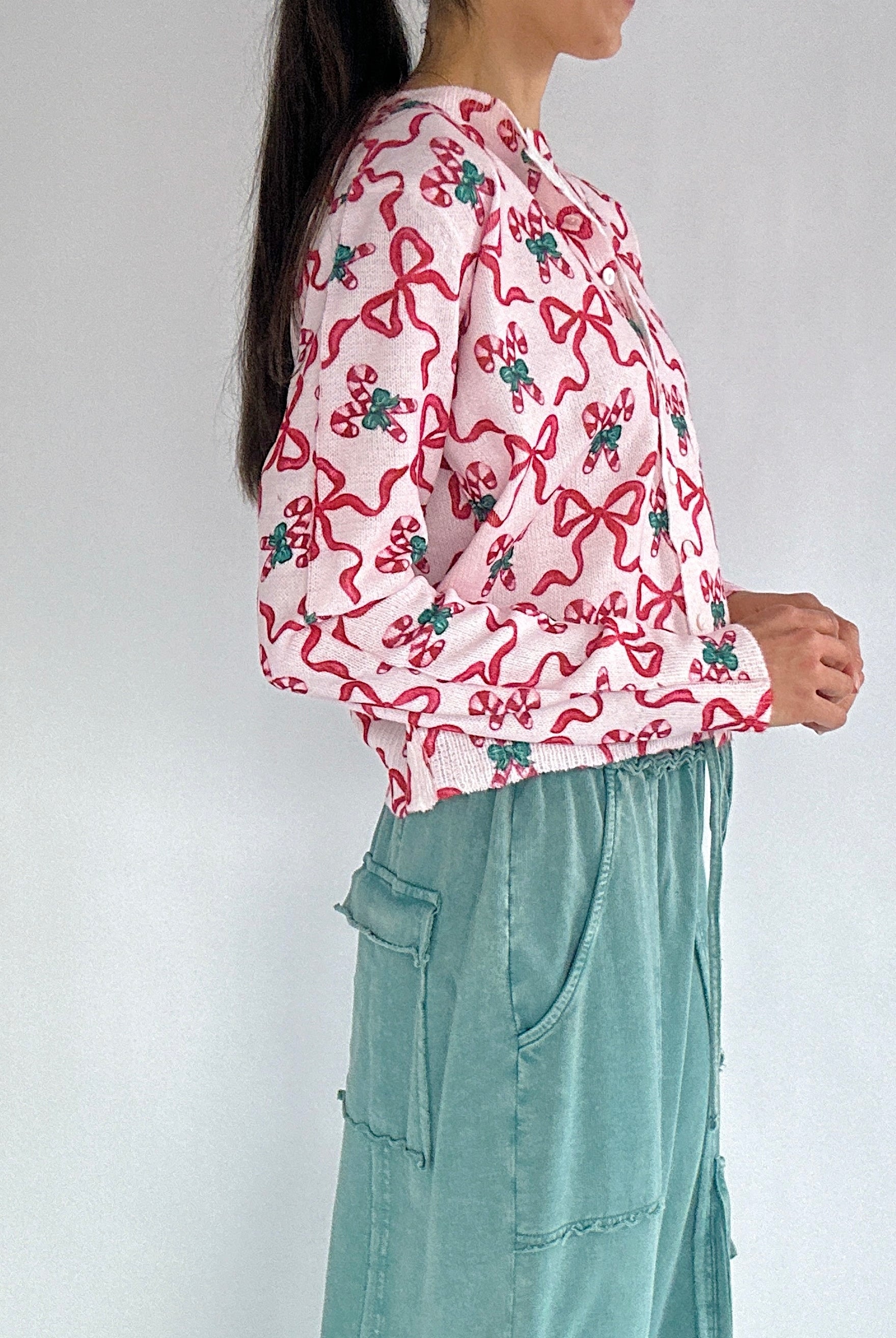 Person wearing a pink candy cane and bow-patterned cardigan from side with a white background