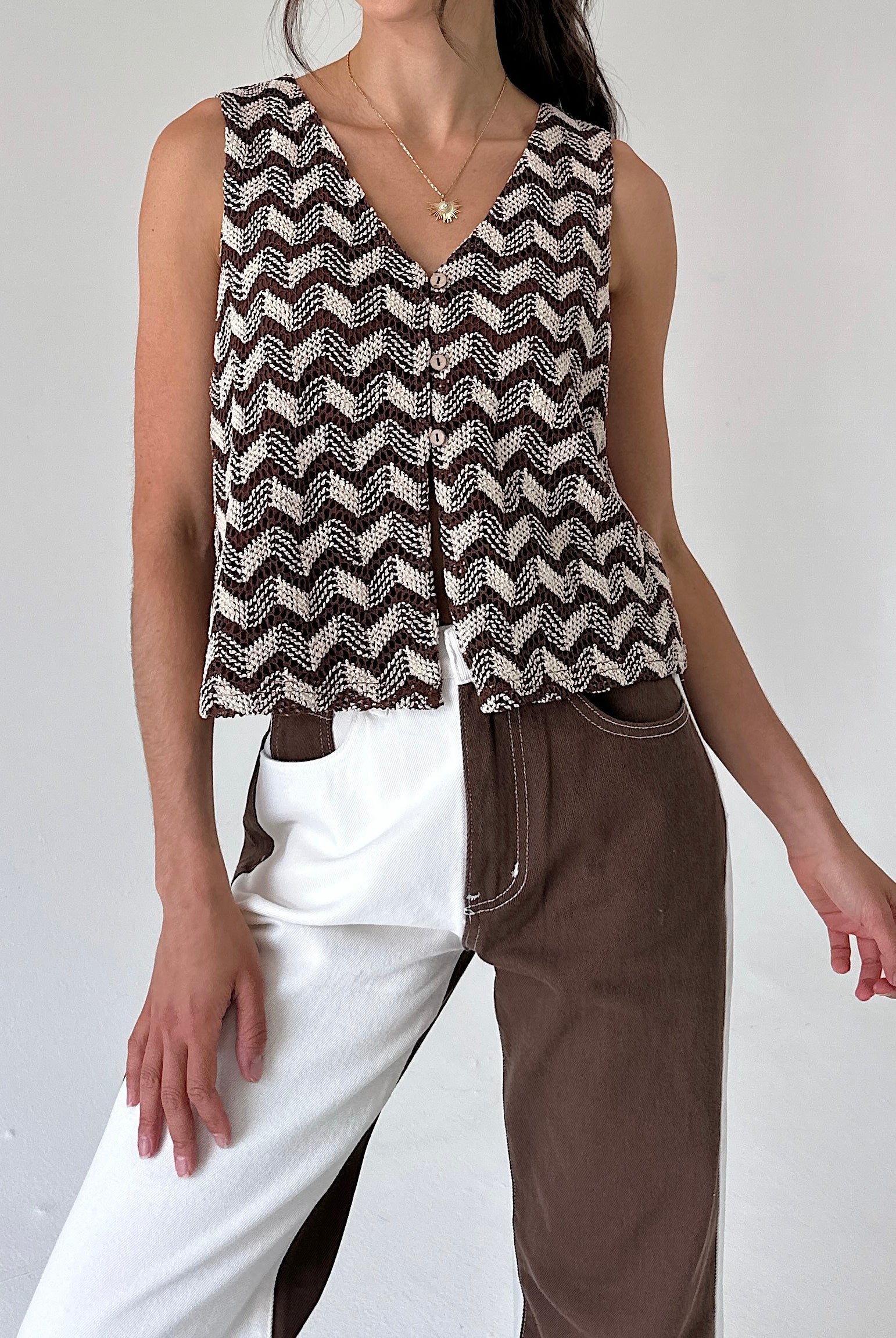 A woman wearing a sleeveless knit top with a brown and beige chevron pattern, styled with split-color pants against a plain light background.