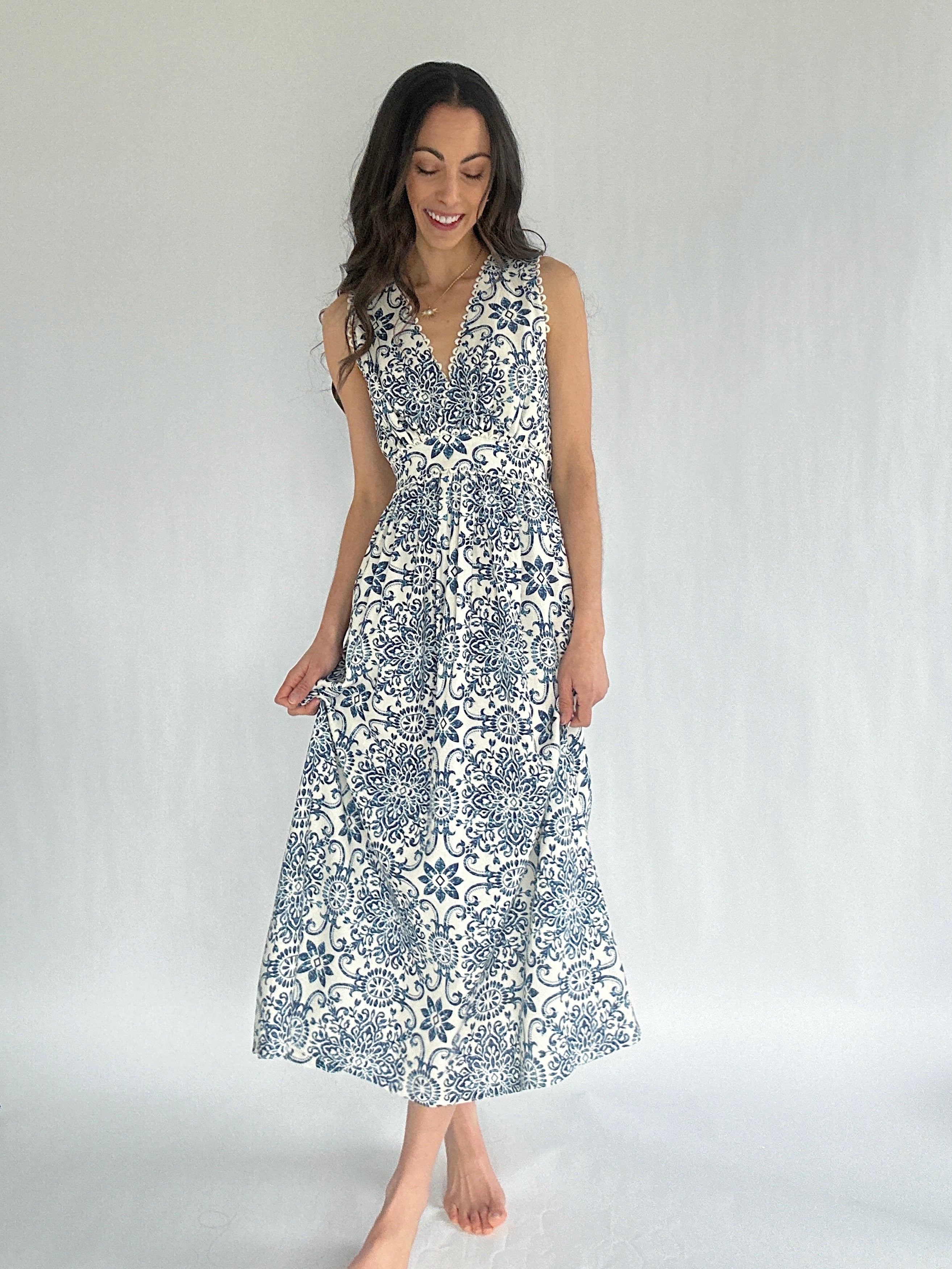 Woman wearing a sleeveless dress with a white and blue pattern against a plain background
