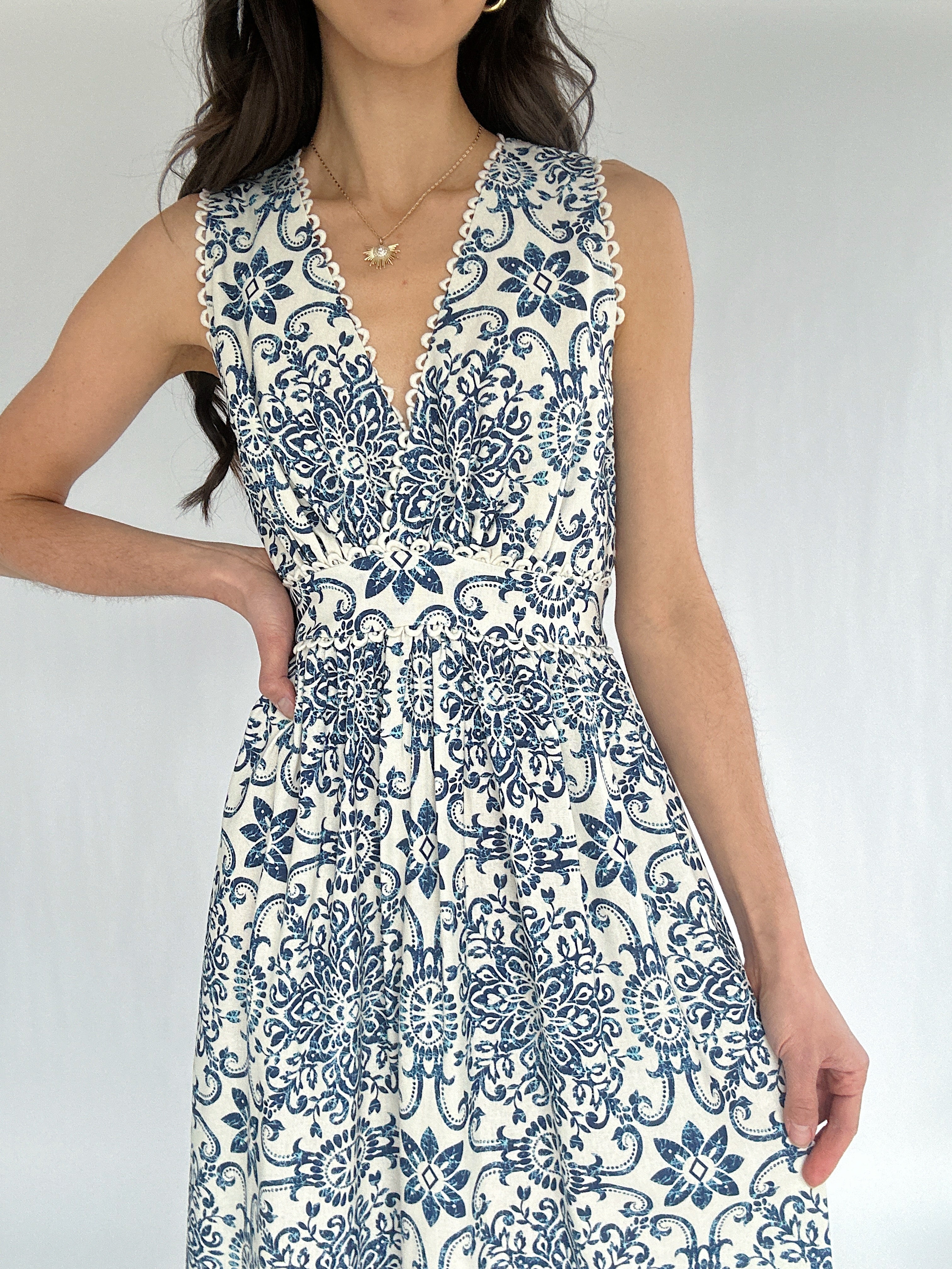 Woman wearing a blue and white patterned dress against a plain background showing v-neckline