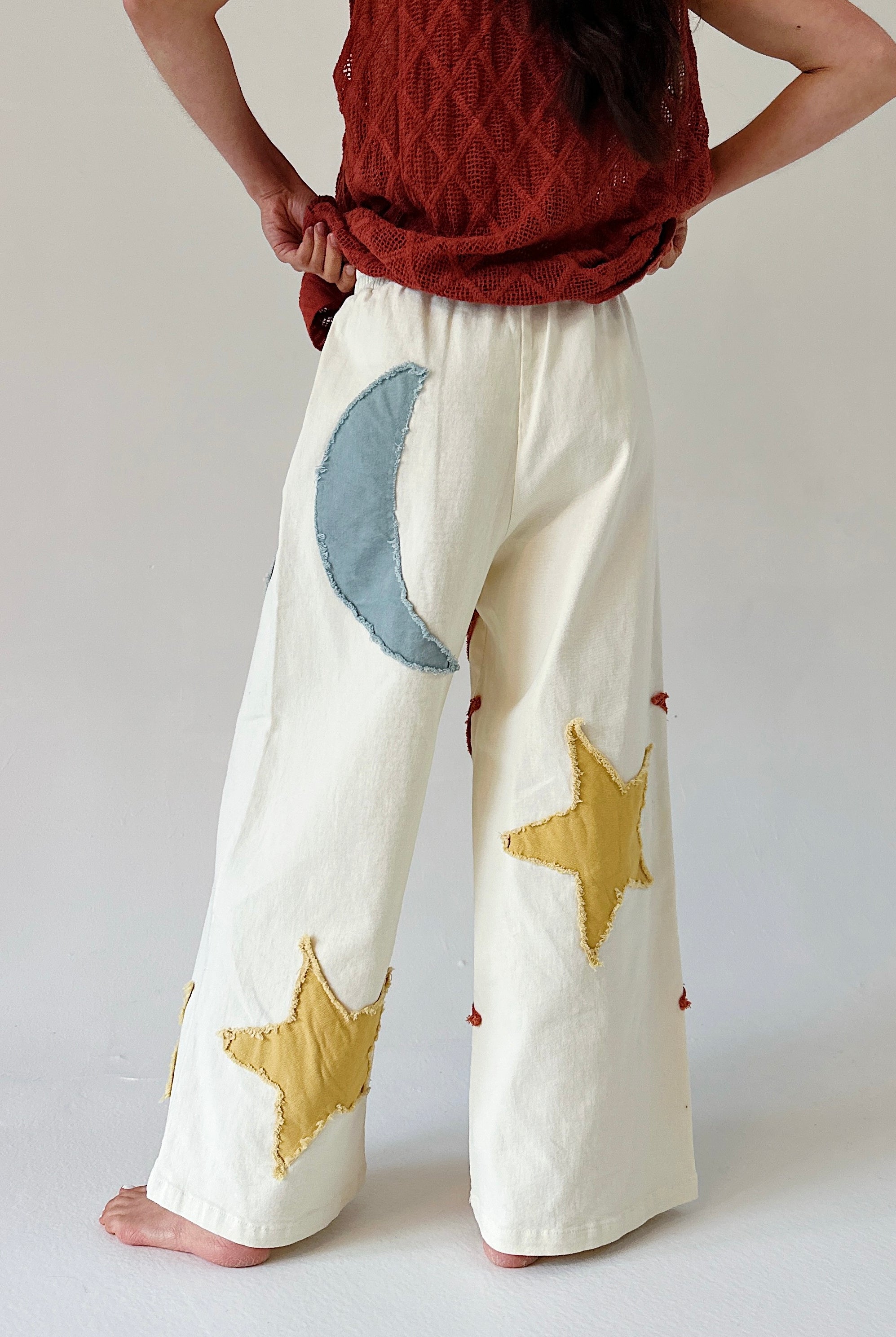 Person wearing white pants with star and moon patches on the back against a plain background