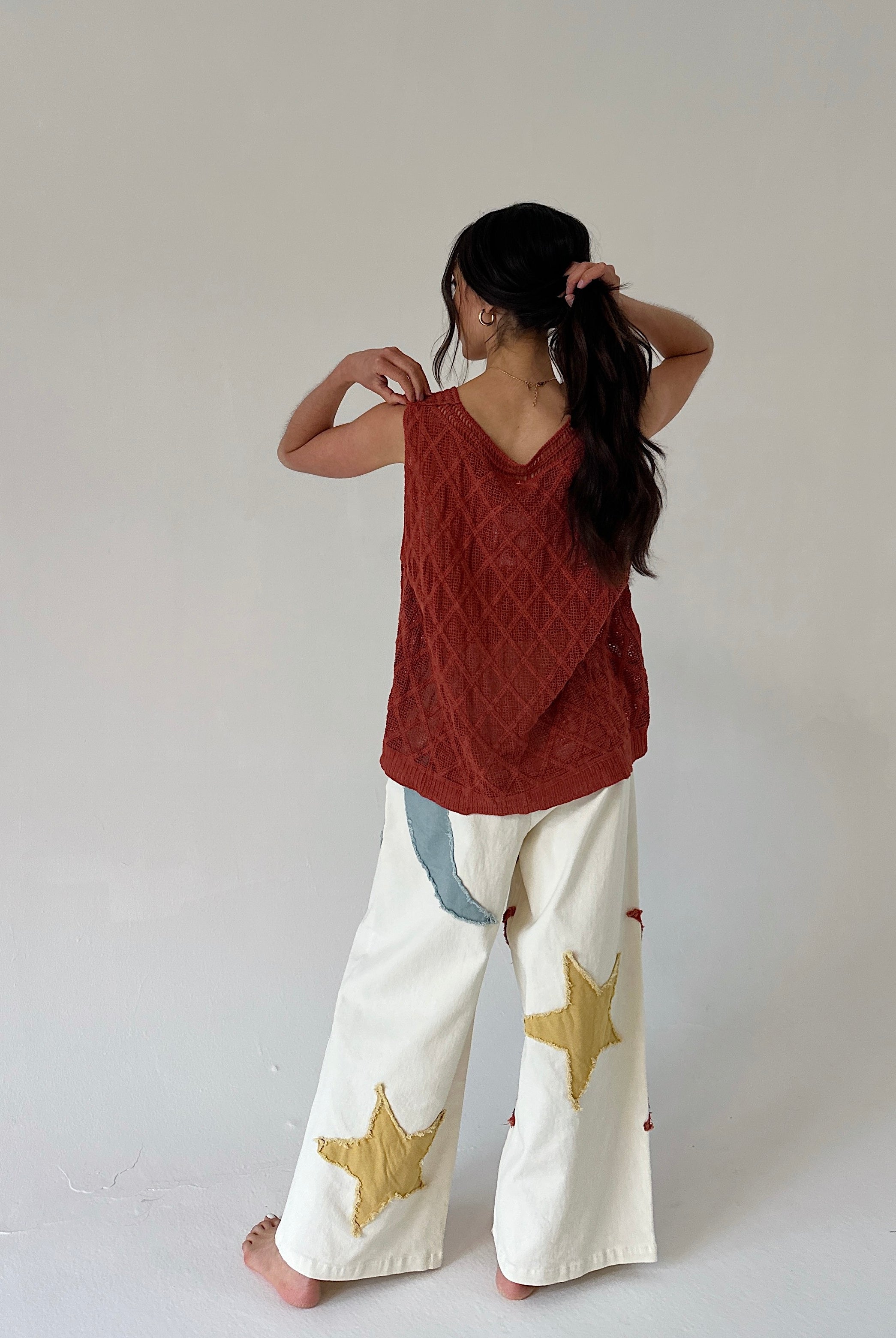 Person wearing a rust-colored sleeveless top and white pants with star patterns on a plain background from back