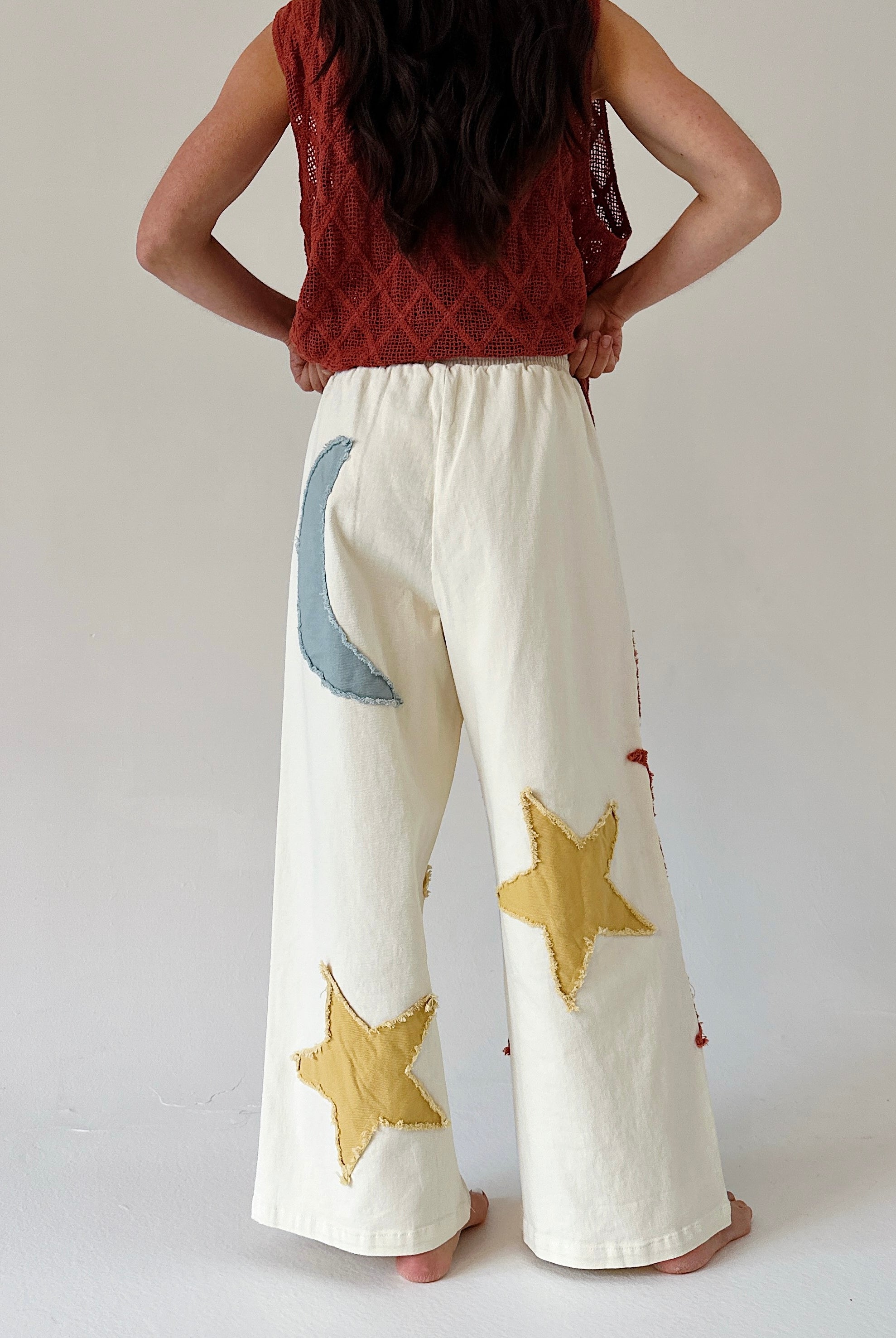 Person wearing white pants with star and moon designs on a plain background