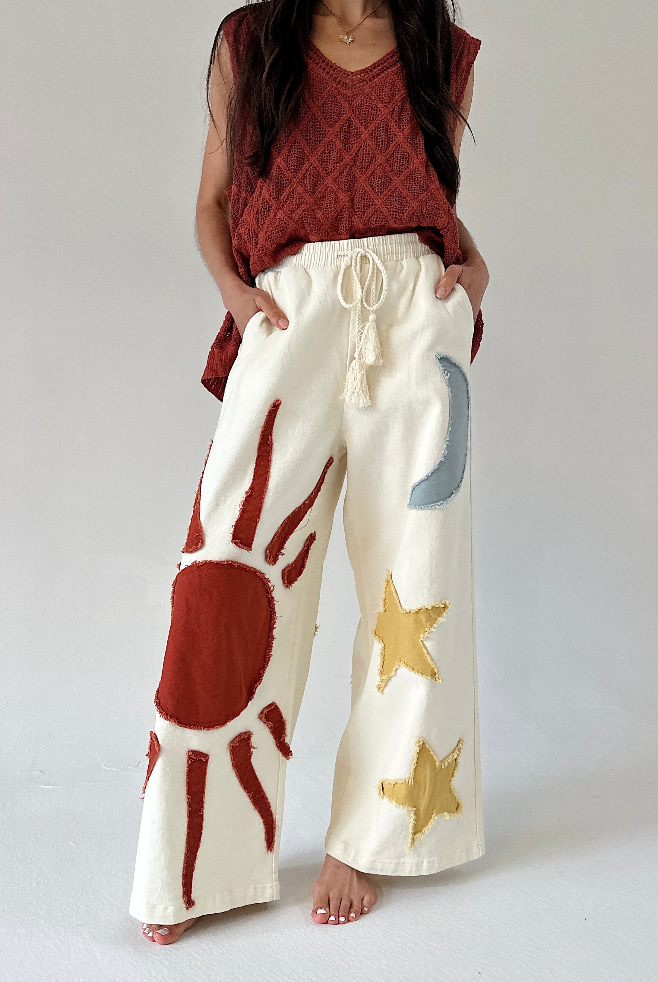 Person wearing cream-colored pants with sun and moon and star designs on a plain background
