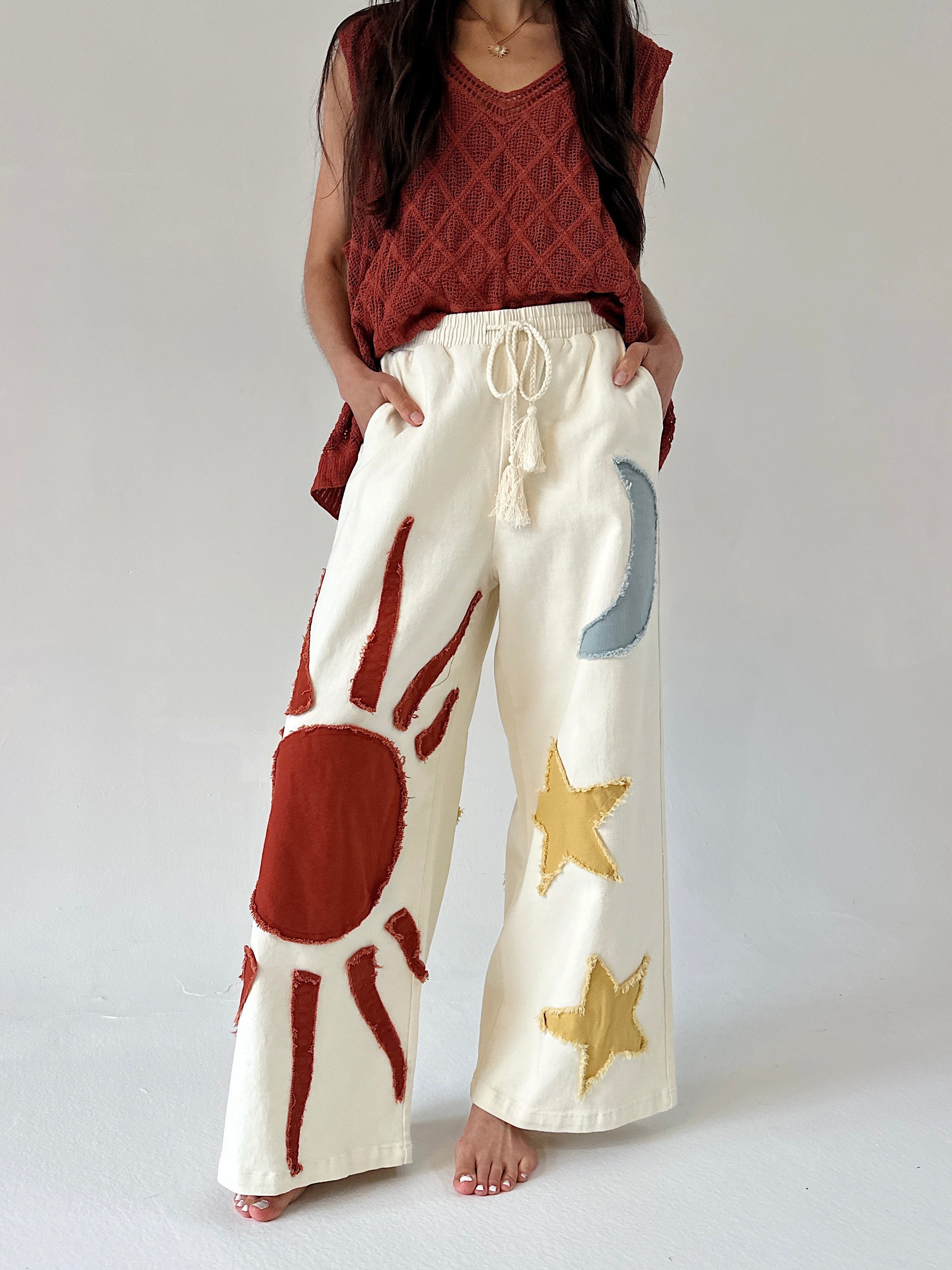 Person wearing cream-colored pants with sun and moon and star designs on a plain background