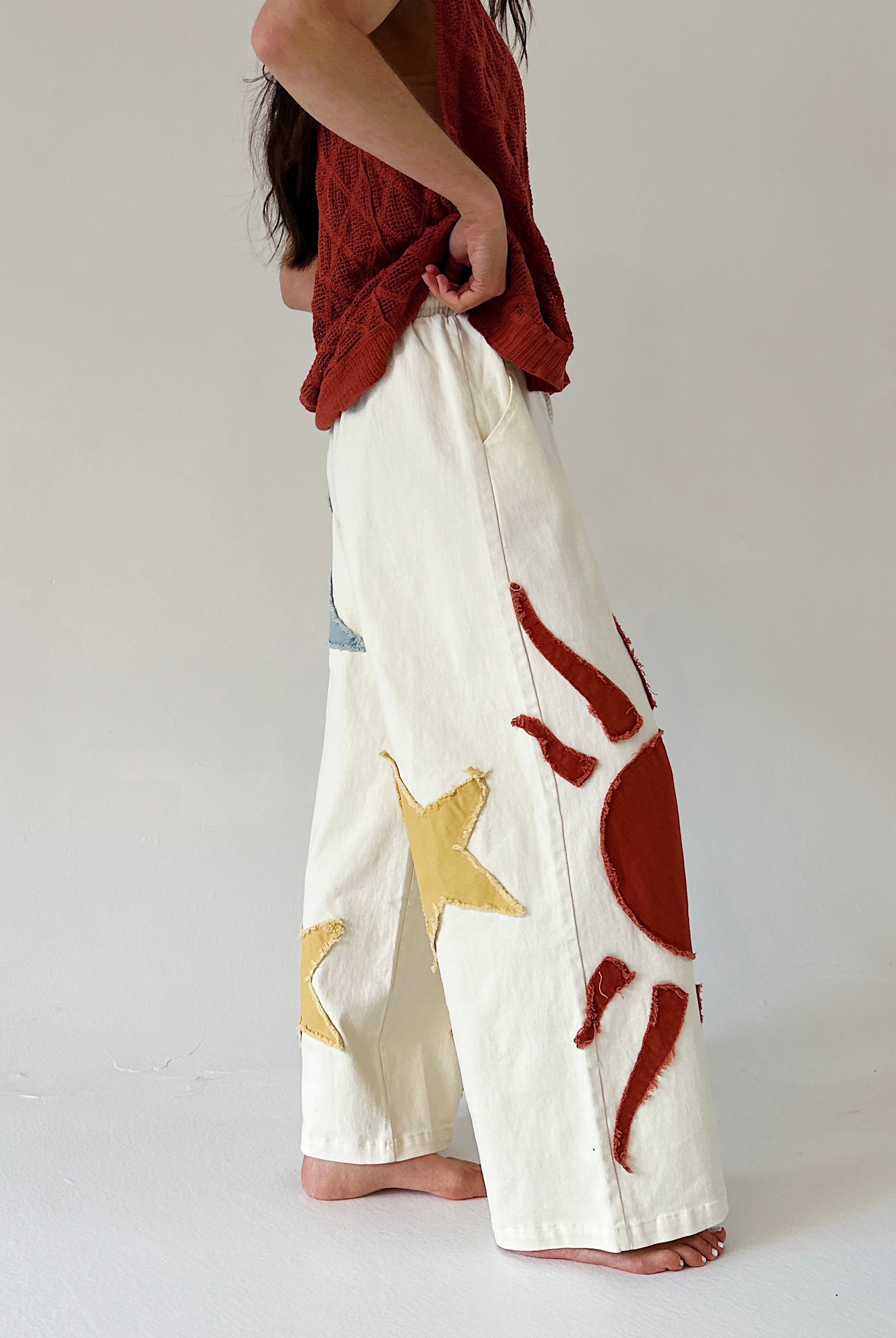 Person wearing white pants with red and gold abstract designs on a plain background
