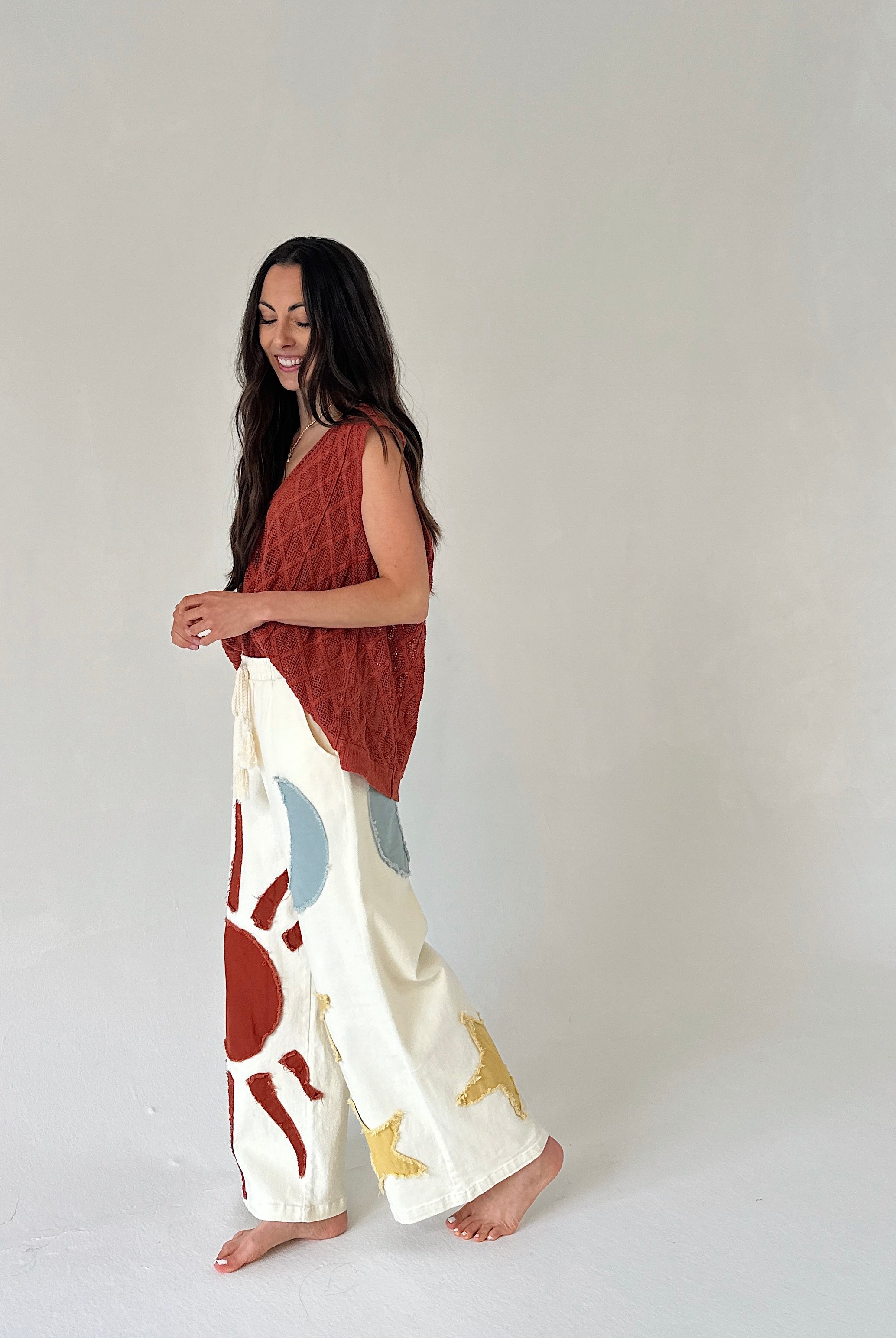 Woman wearing a rust-colored top and white pants with abstract patterns on a plain background