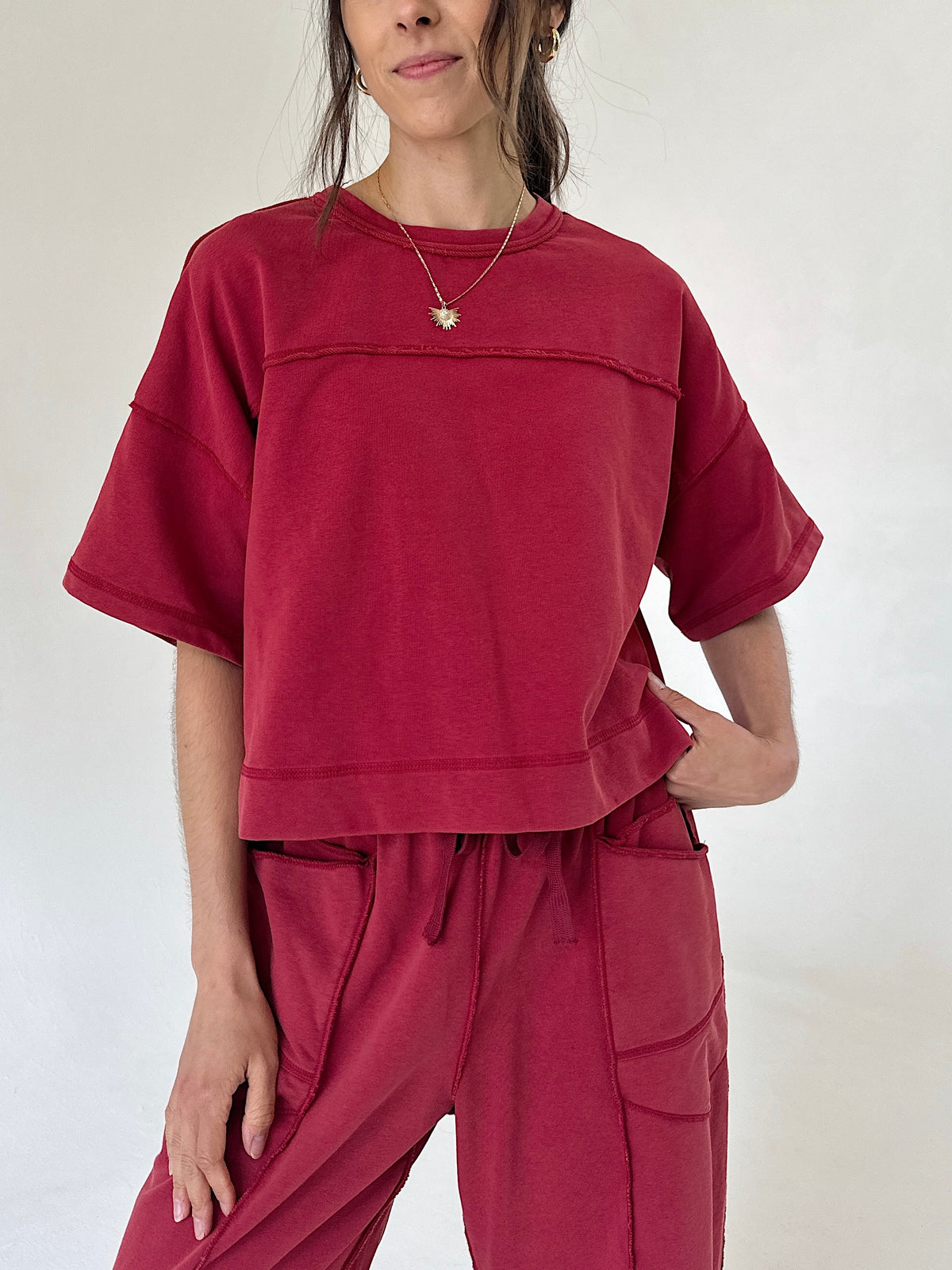 A woman wearing a cropped short-sleeve t-shirt and matching drawstring pants in a washed deep red or burgundy color, photographed against a plain off-white studio background.