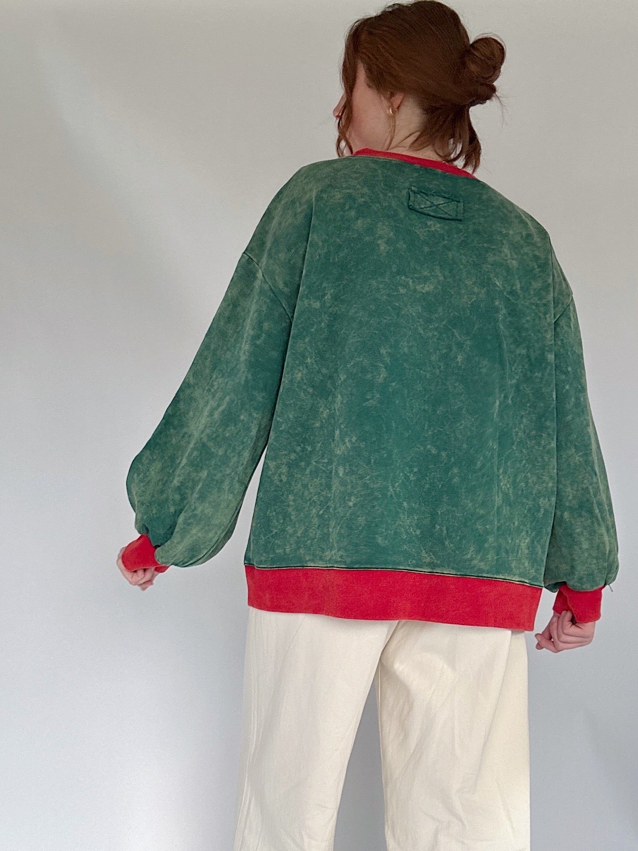 Person wearing a green and red pullover with white pants against a plain background showing back