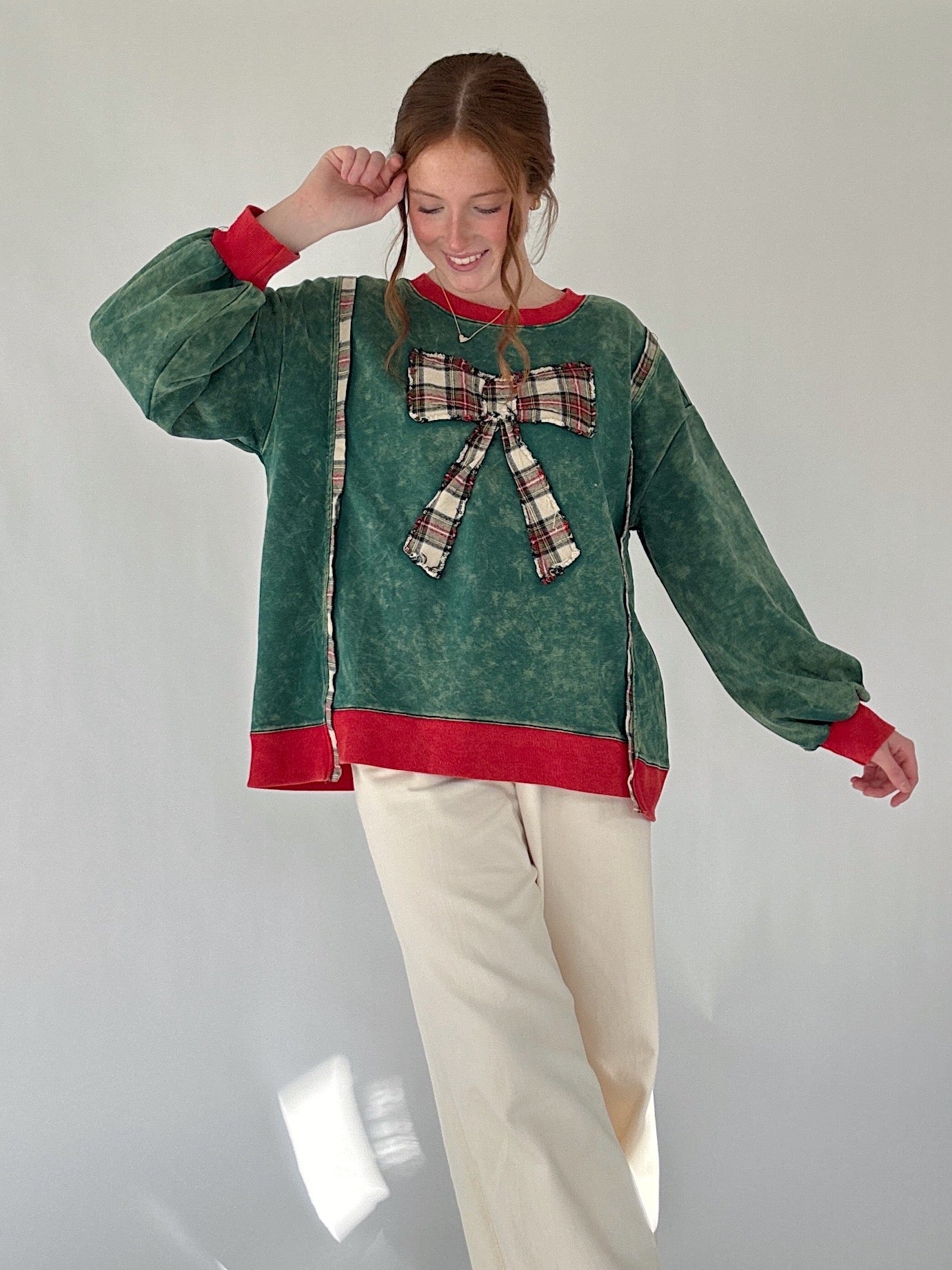 Person wearing a green pullover with a plaid bow and red trim on a plain background