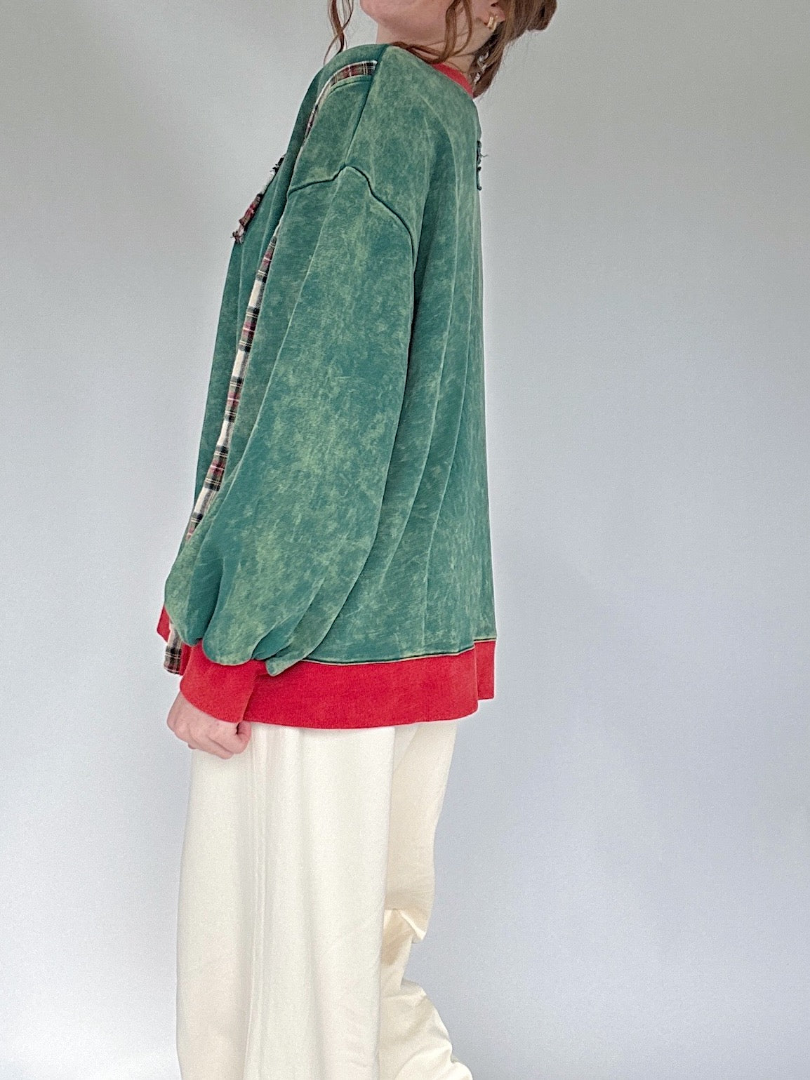 Person wearing a green and red top with white pants against a plain background showing side