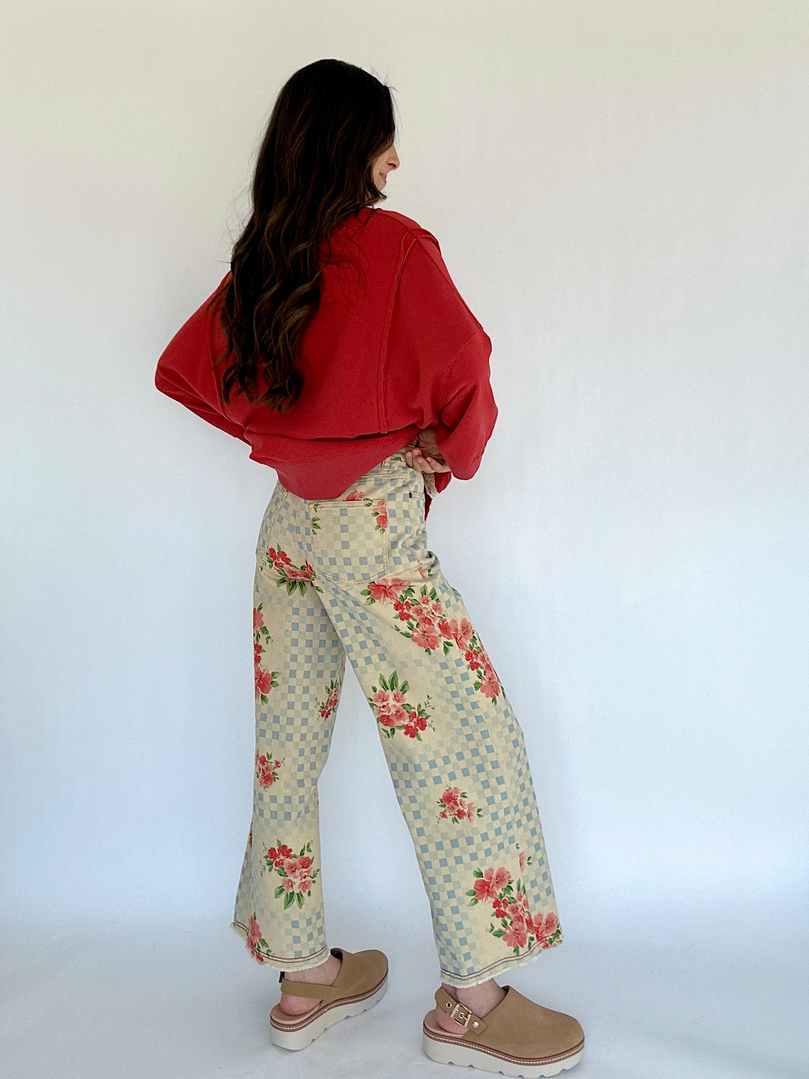 Person wearing a red sweatshirt and floral pants against a white background