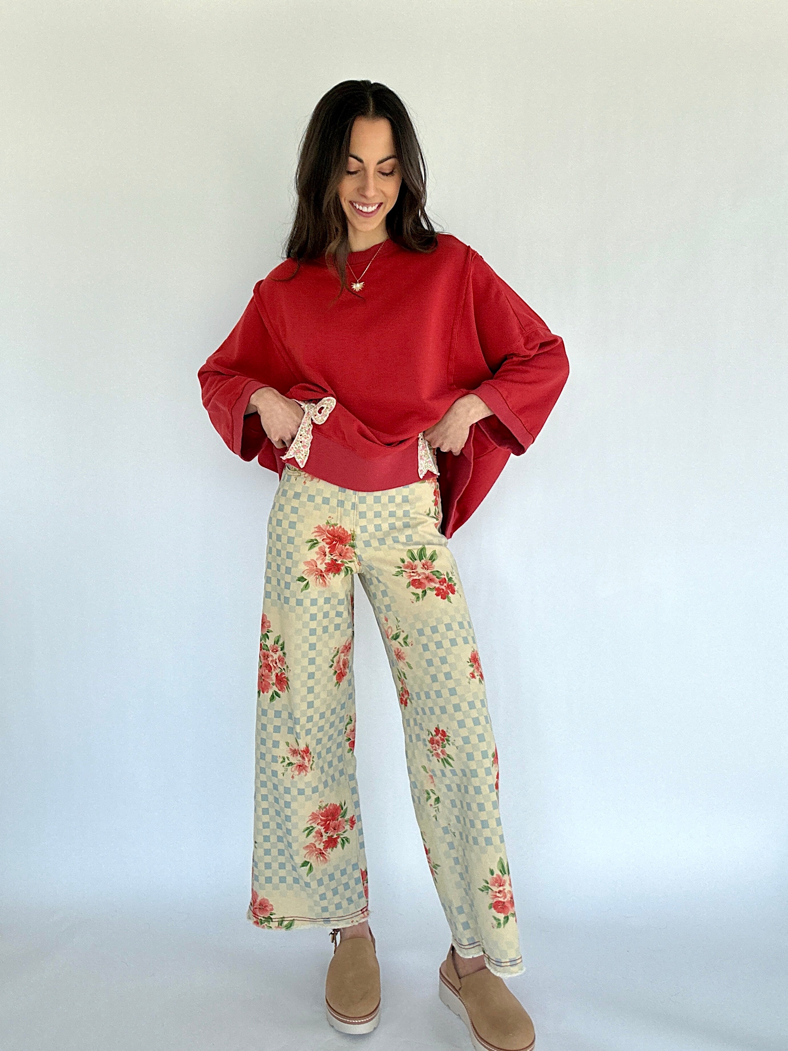 Woman wearing a red sweater and floral and checkered patterned pants against a white background