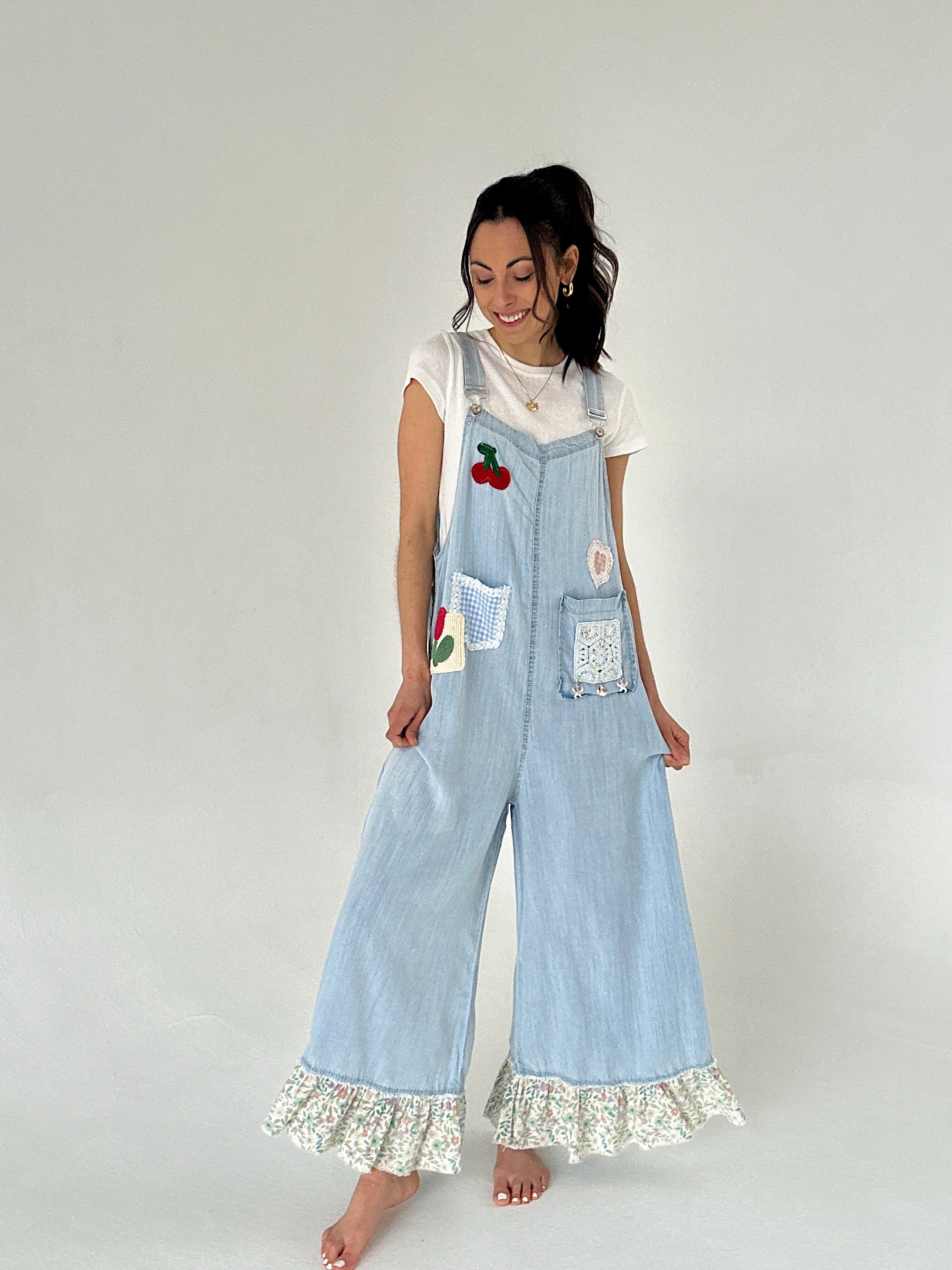 Woman wearing light blue denim overalls with floral hem on a white background