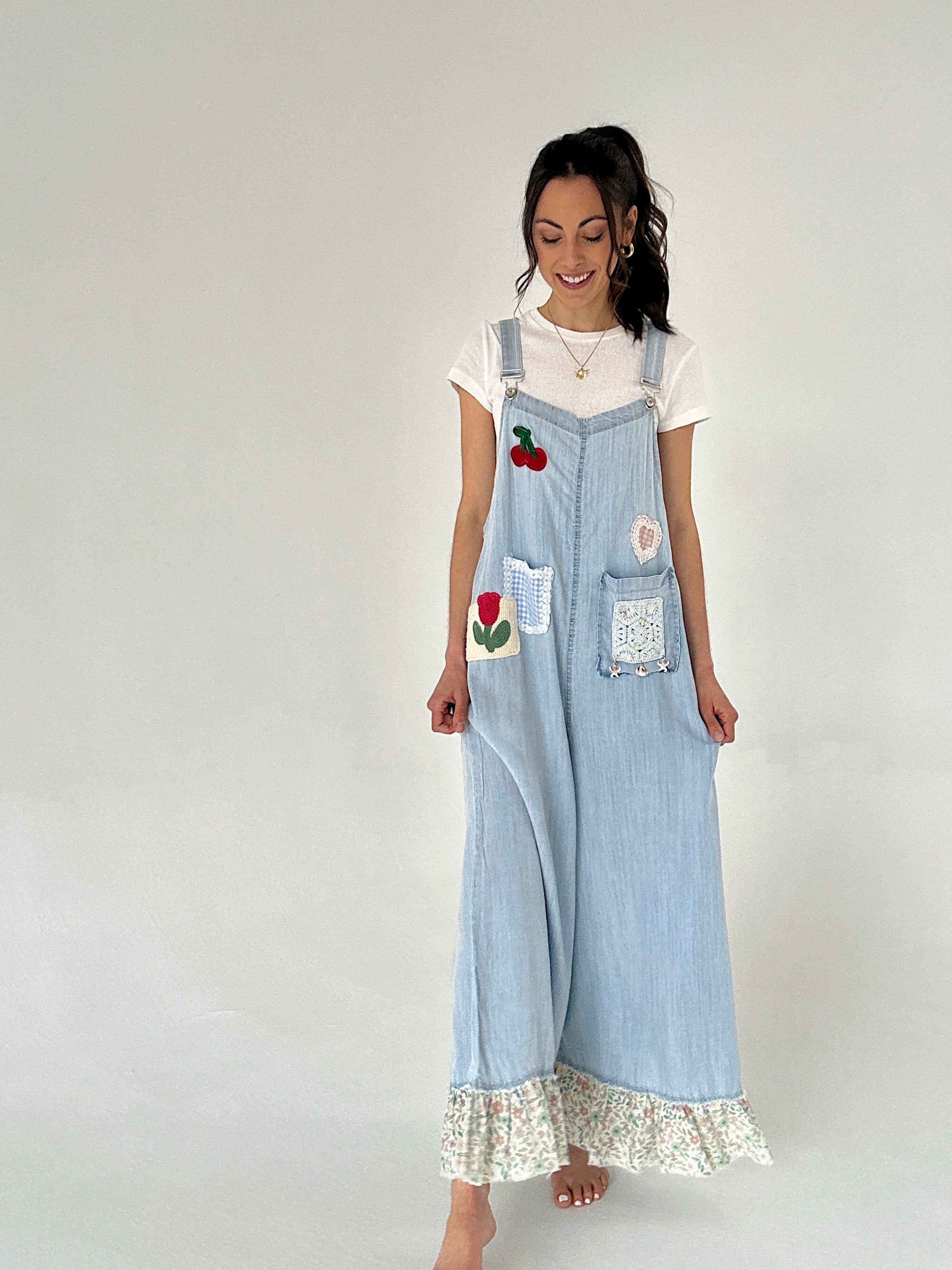 Woman wearing light blue denim overalls with floral lace trim on a white background
