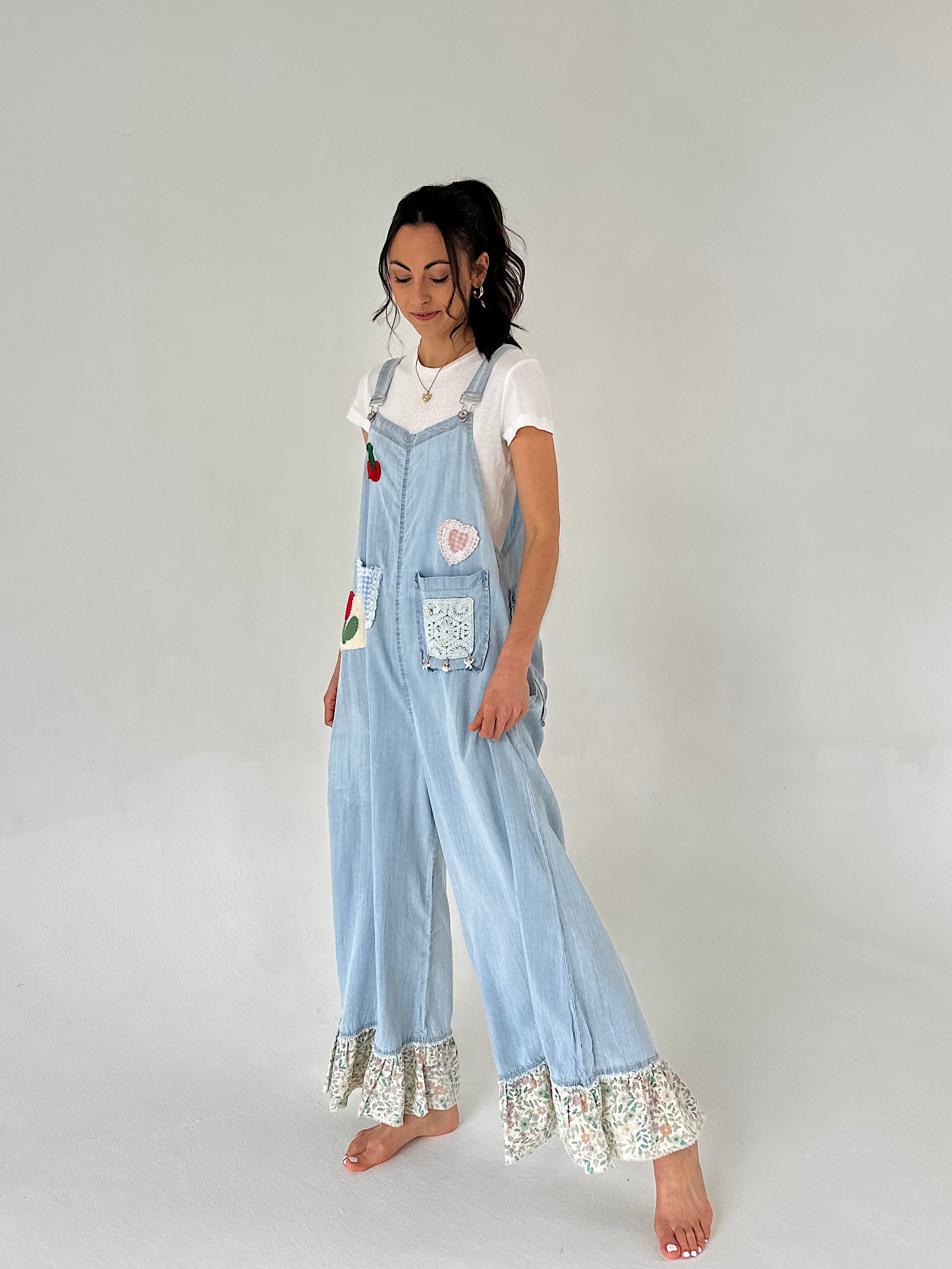 Woman wearing light blue denim overalls with lace trim on a plain background