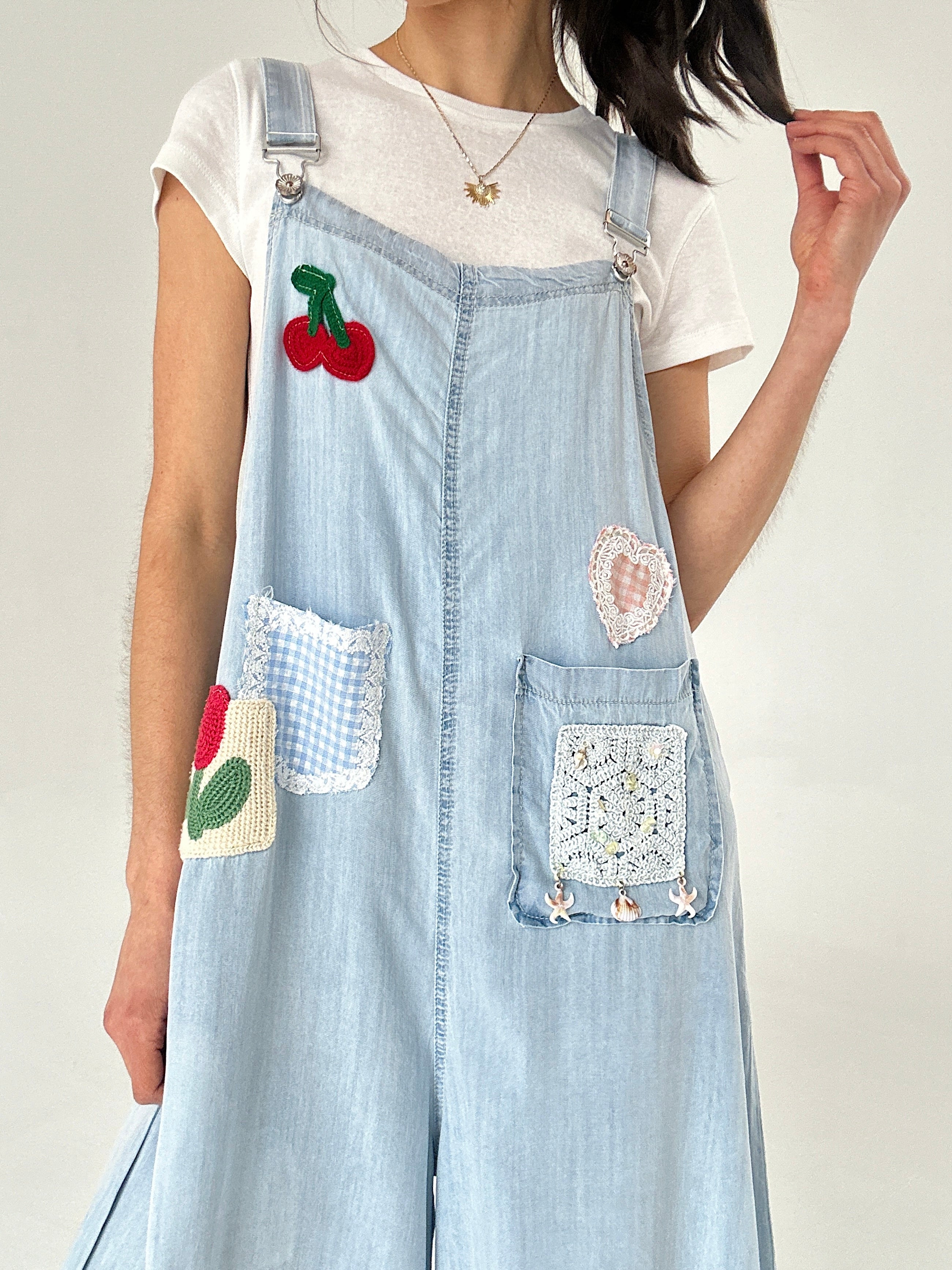 Light blue denim overalls with embroidered patches on a plain background
