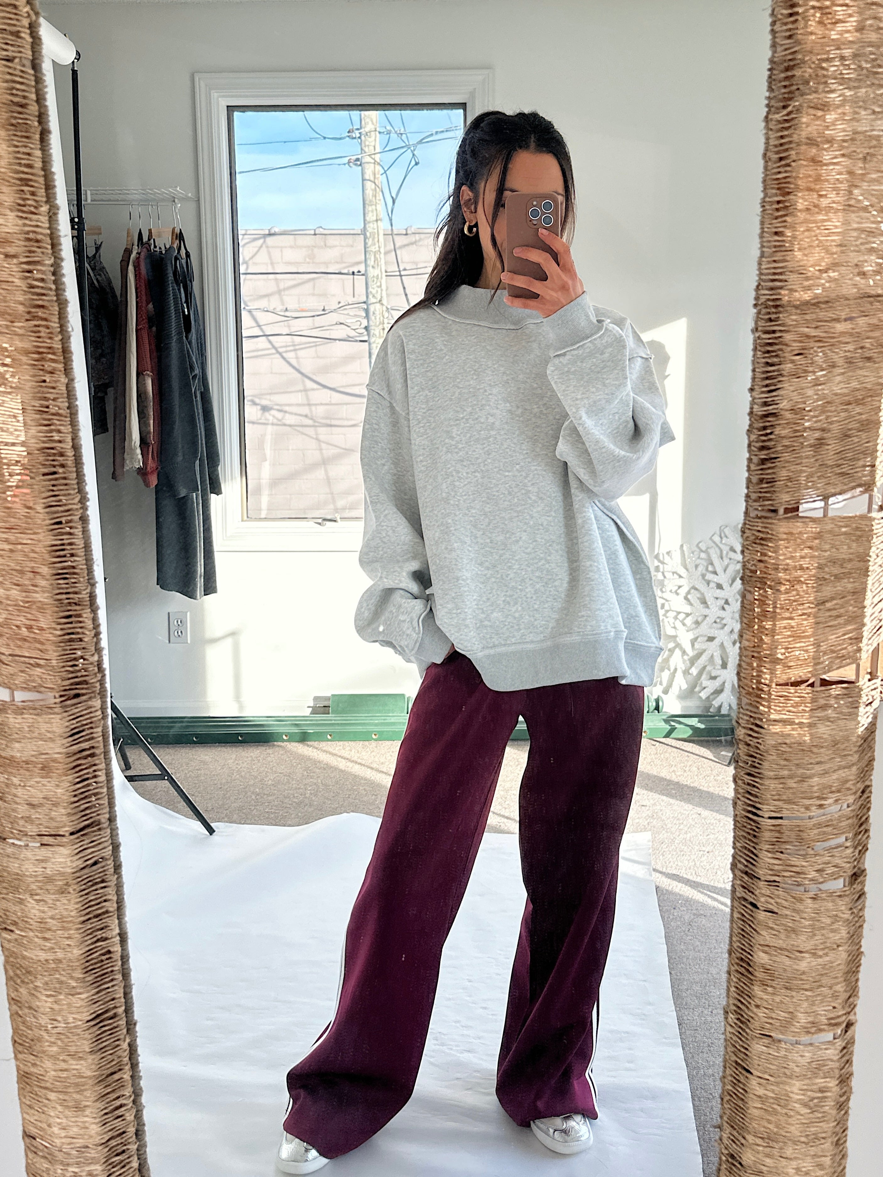 Person wearing a gray sweatshirt and maroon pants taking a mirror selfie.
