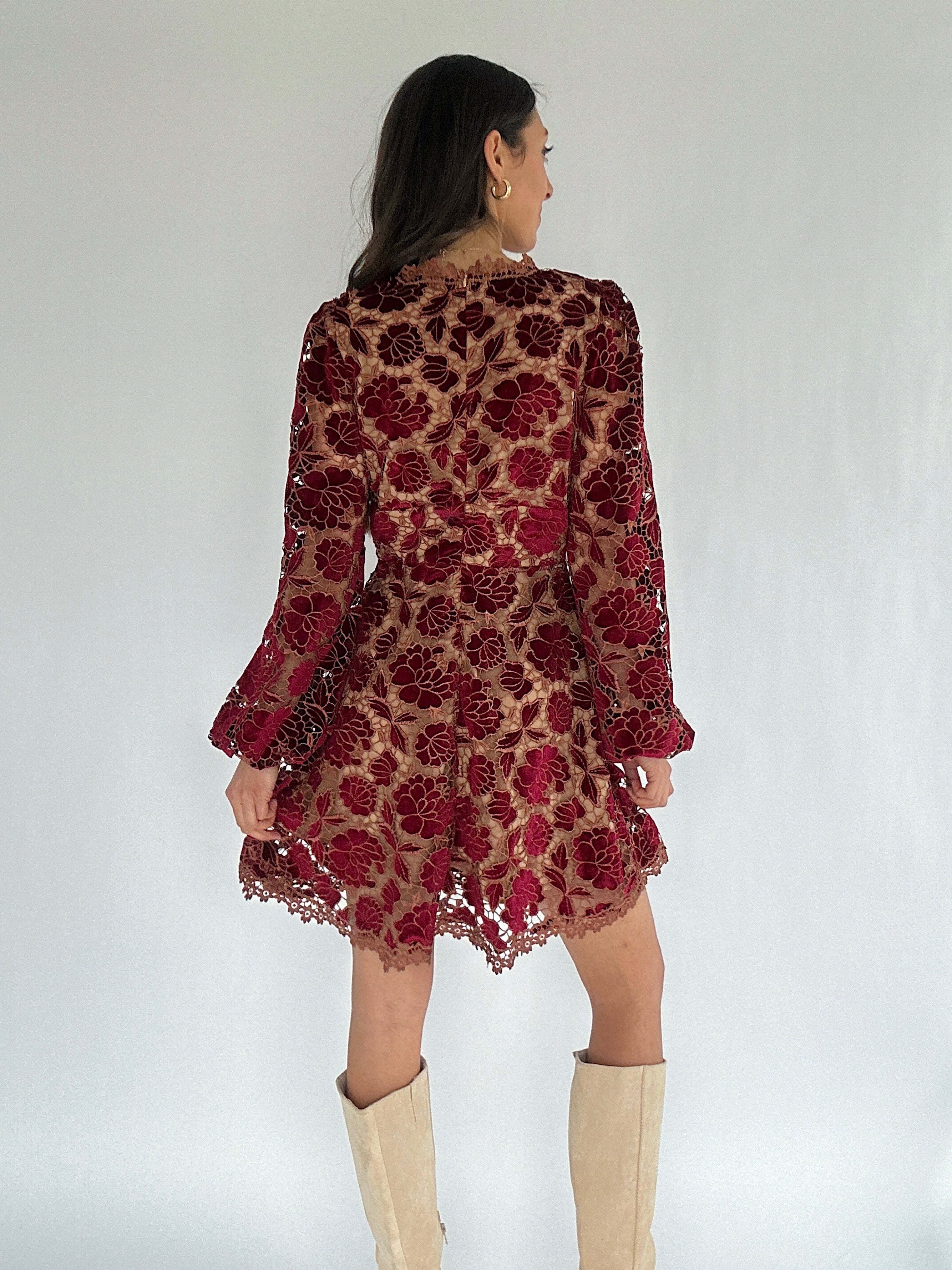 Woman wearing a red floral lace dress with beige knee-high boots on a white background