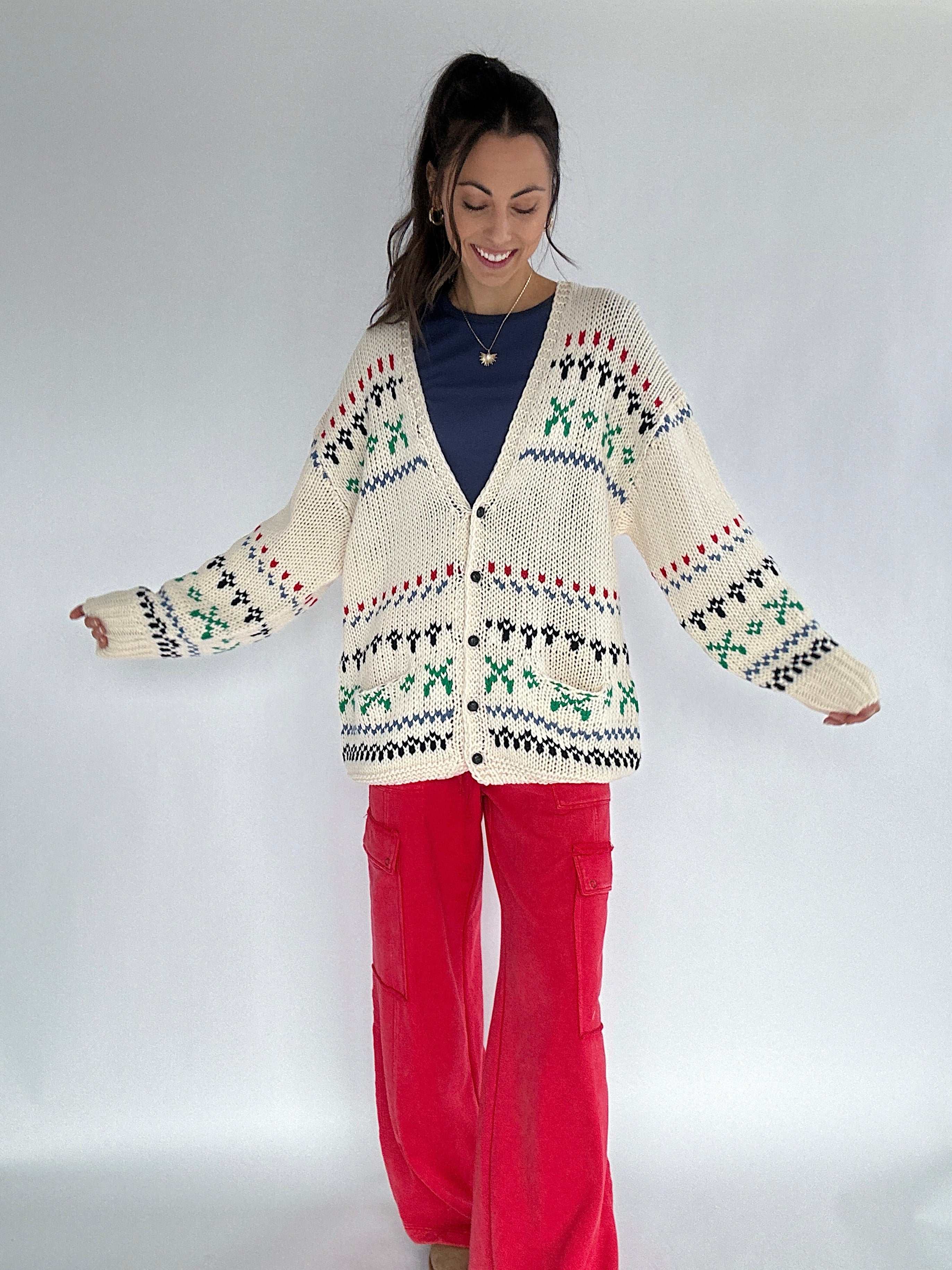 Woman wearing a patterned knit cardigan and red pants on a white background