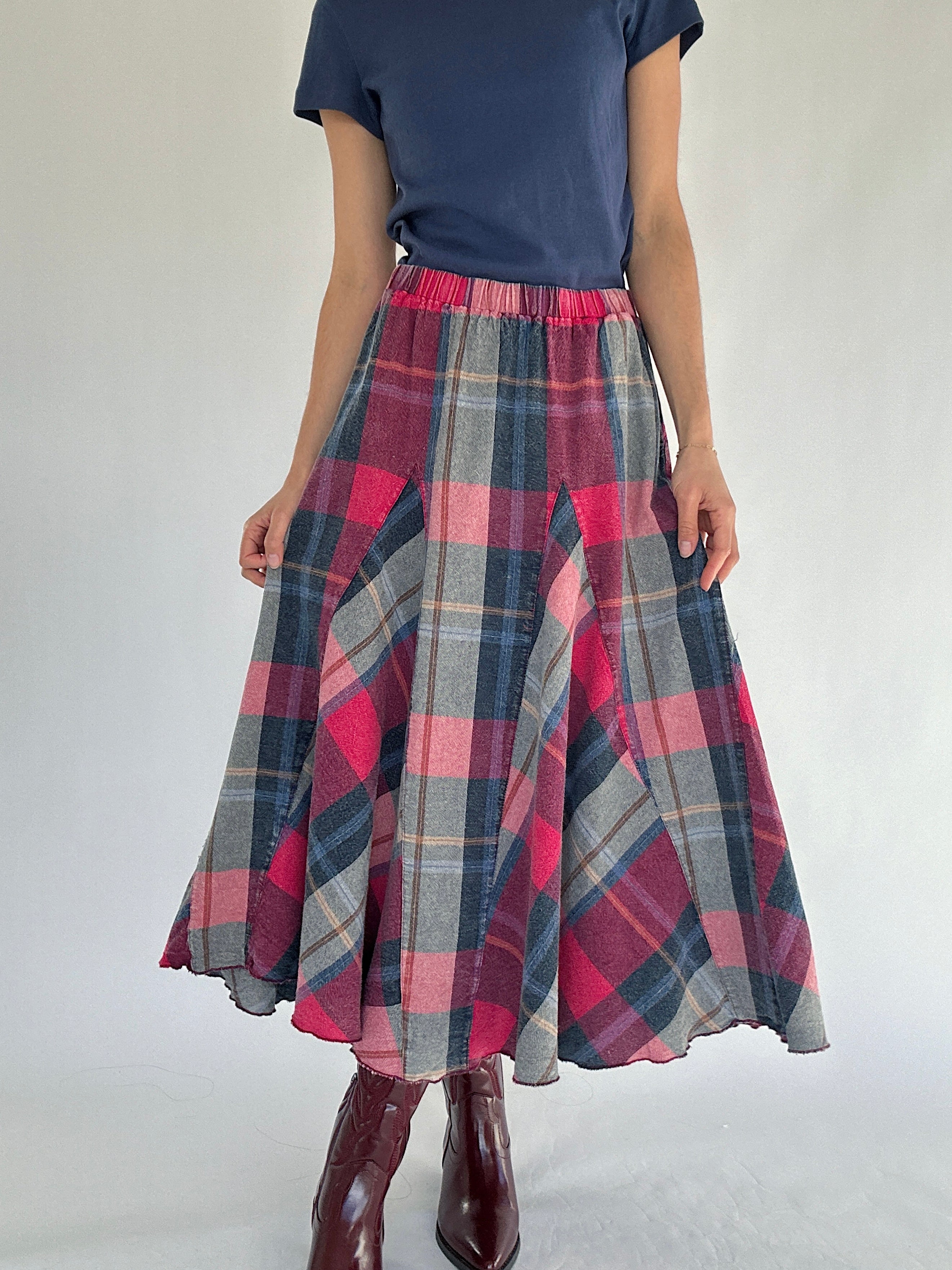 Person wearing a plaid maxi skirt and blue tee with a plain background