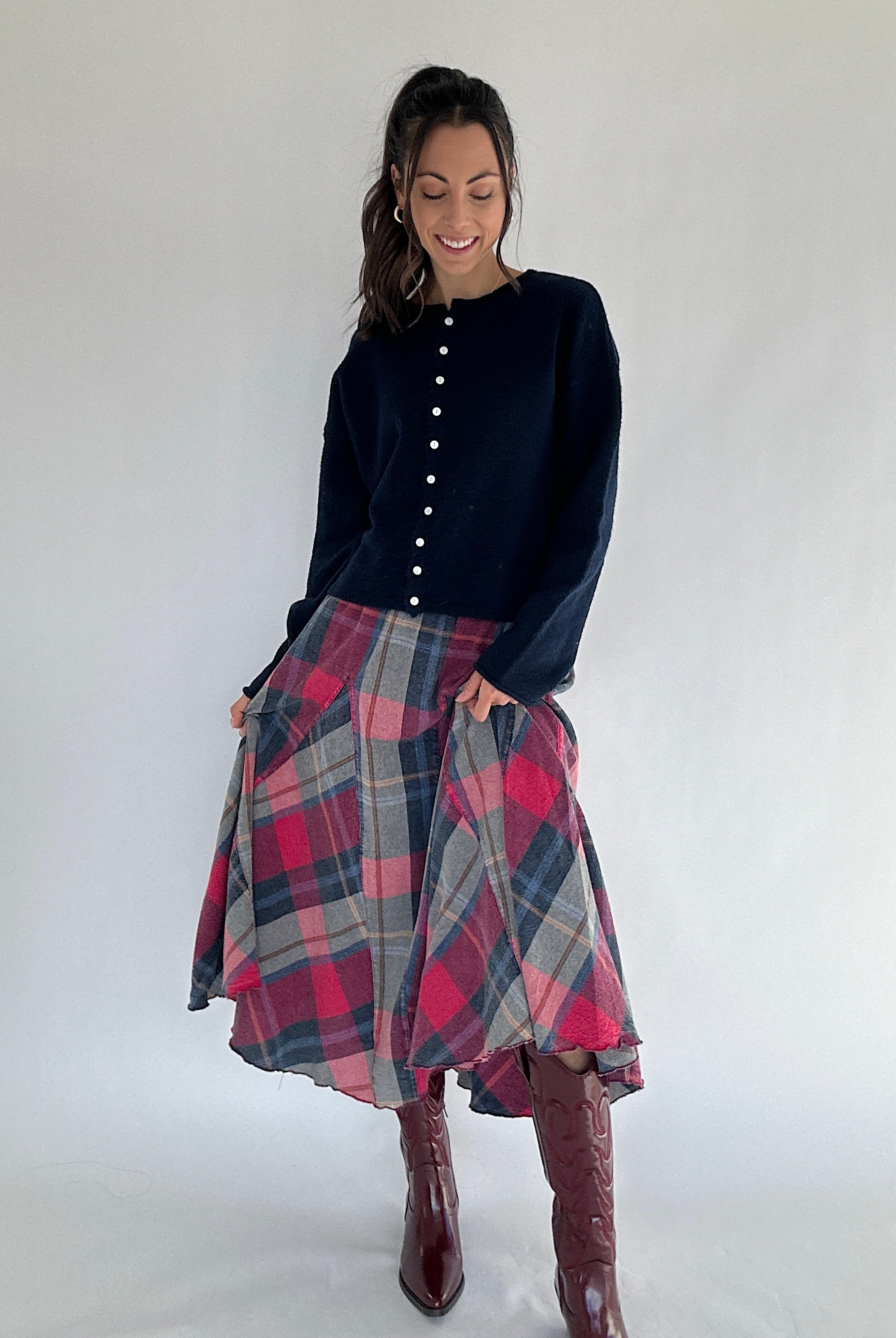 Woman wearing a navy cardigan top and plaid skirt with burgundy boots on a white background