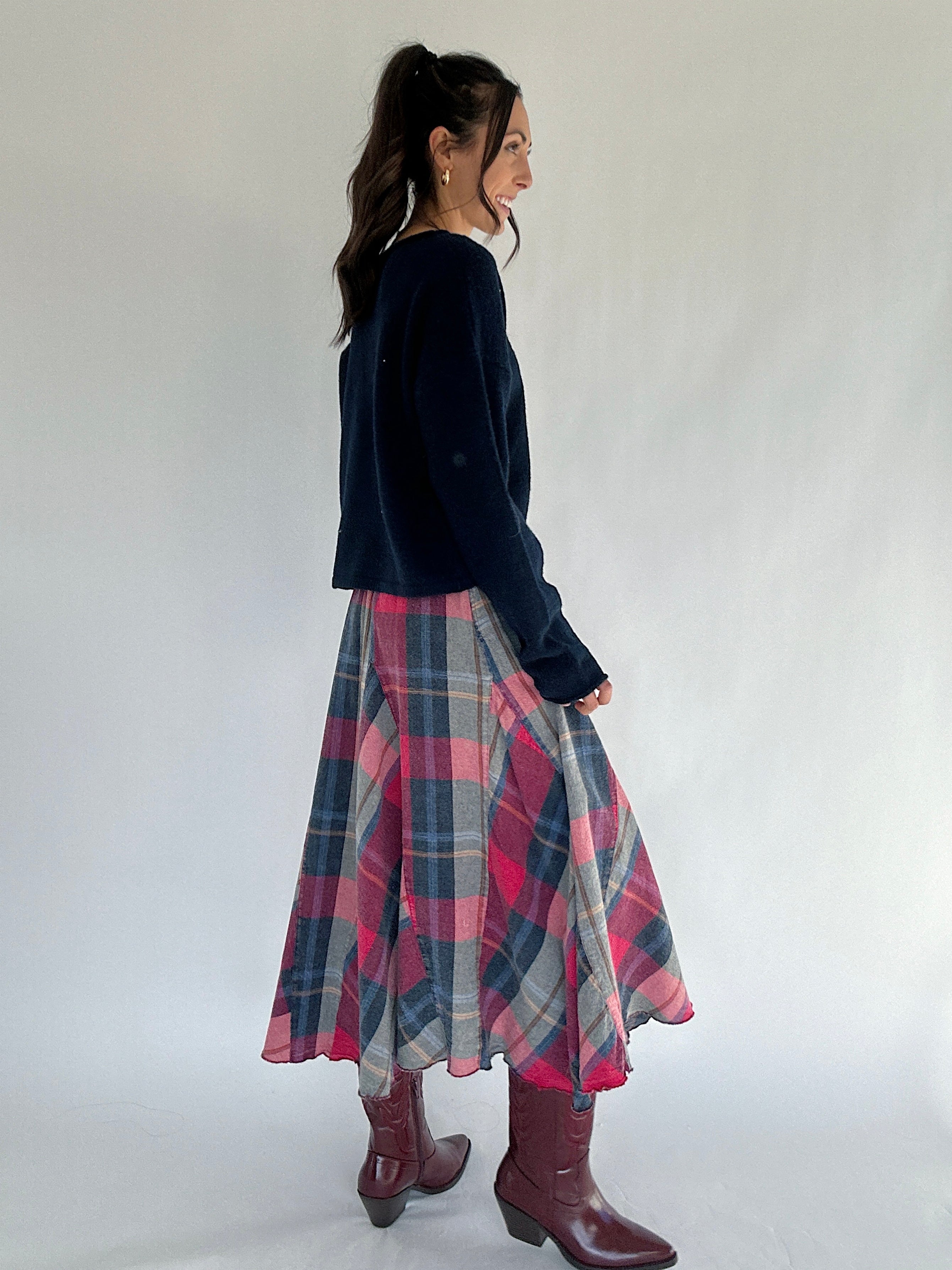 Woman wearing a navy sweater and plaid skirt with maroon boots on a white background