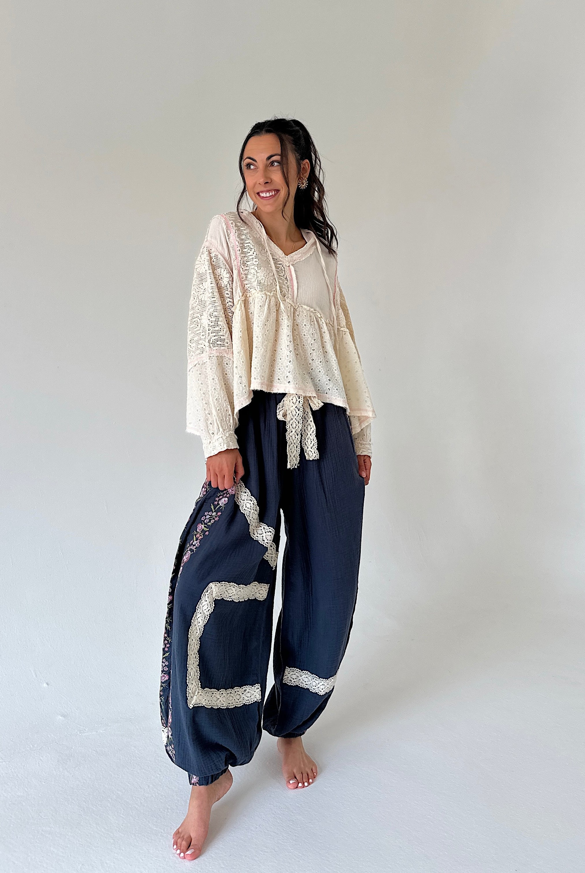 A woman modeling a bohemian-style outfit consisting of a cream lace-trimmed long-sleeve top and navy blue harem pants with cream lace trim, standing against a plain white studio background.