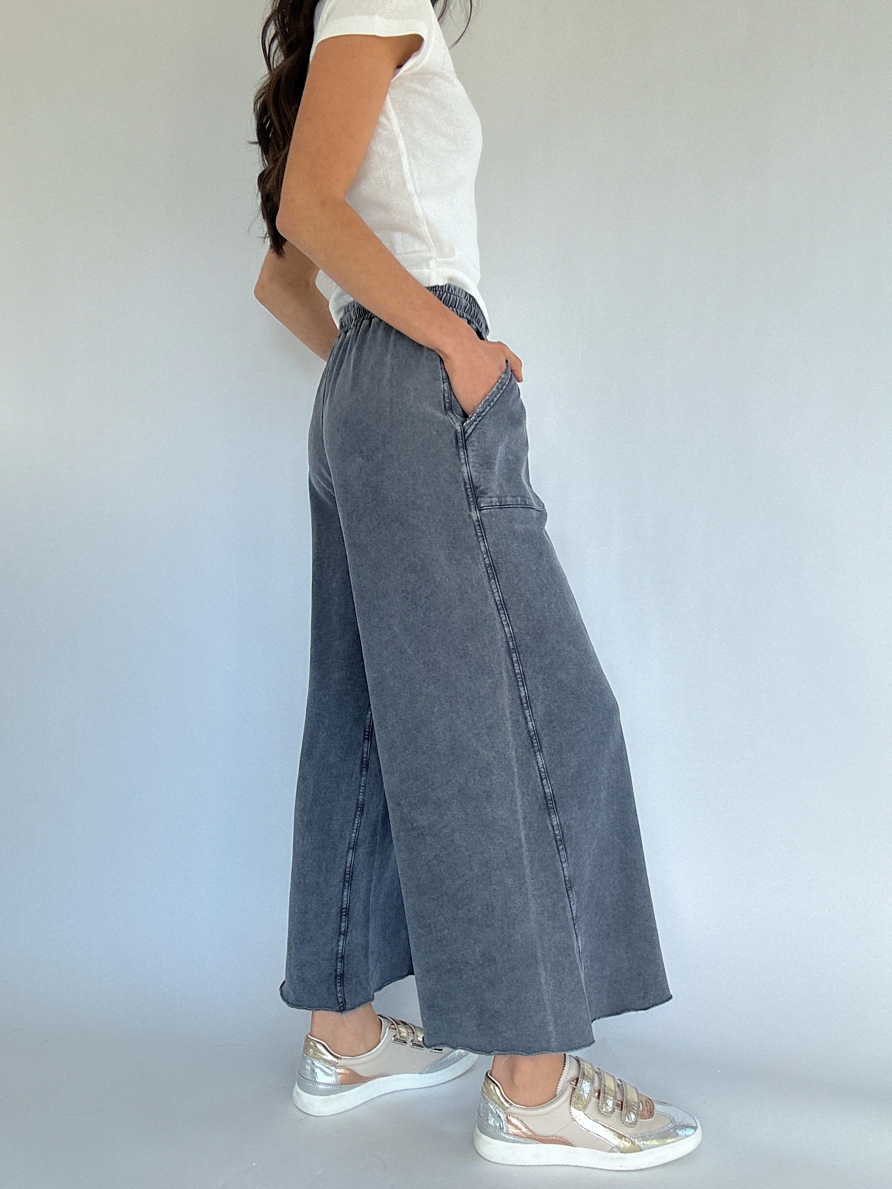 Person wearing gray wide-leg sweatpants and a white top against a plain background showing side pockets