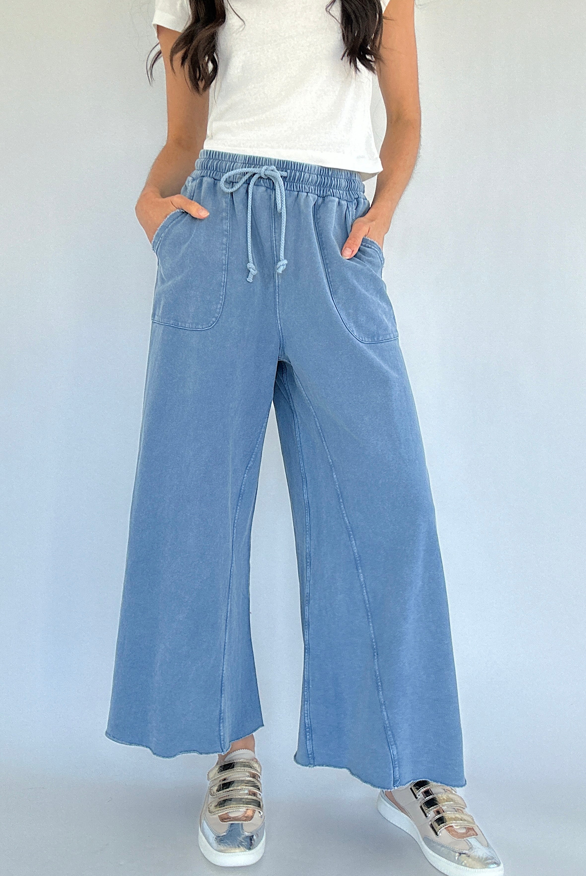 Person wearing light blue wide-leg sweatpants with a white top on a plain background