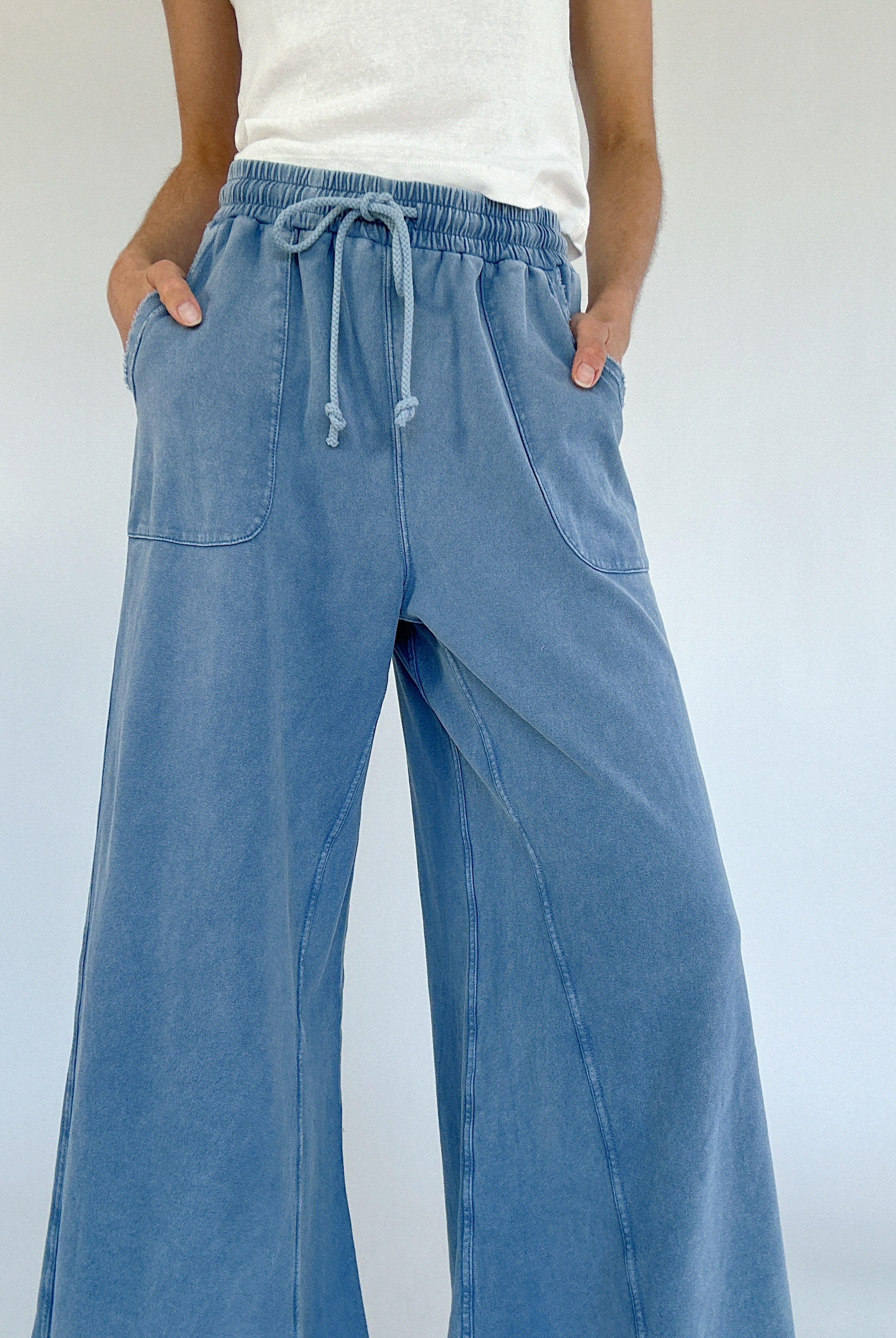 Person wearing blue wide-leg pants with a white background showing drawstring waist and pockets