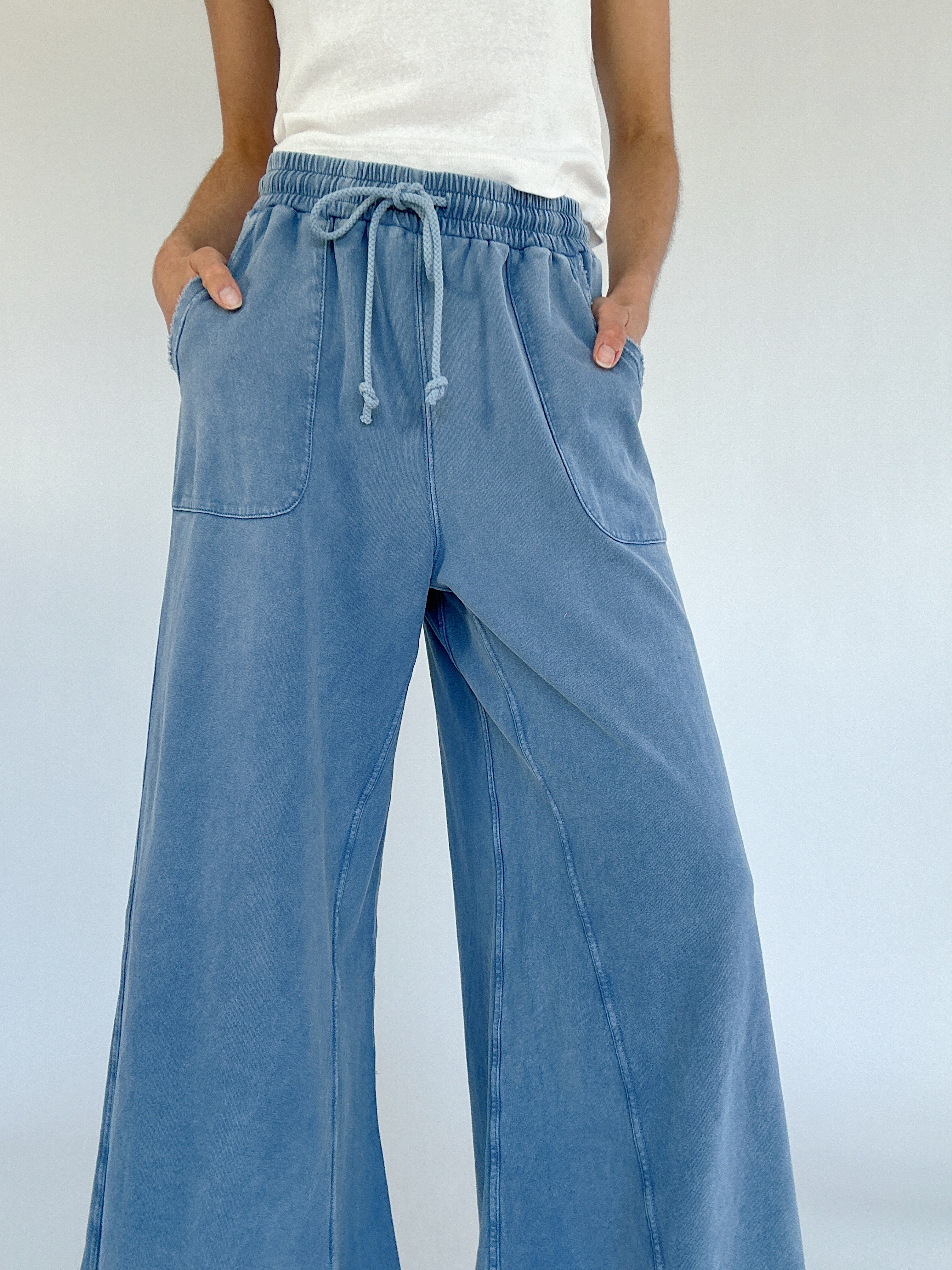 Person wearing blue wide-leg pants with a white background showing drawstring waist and pockets