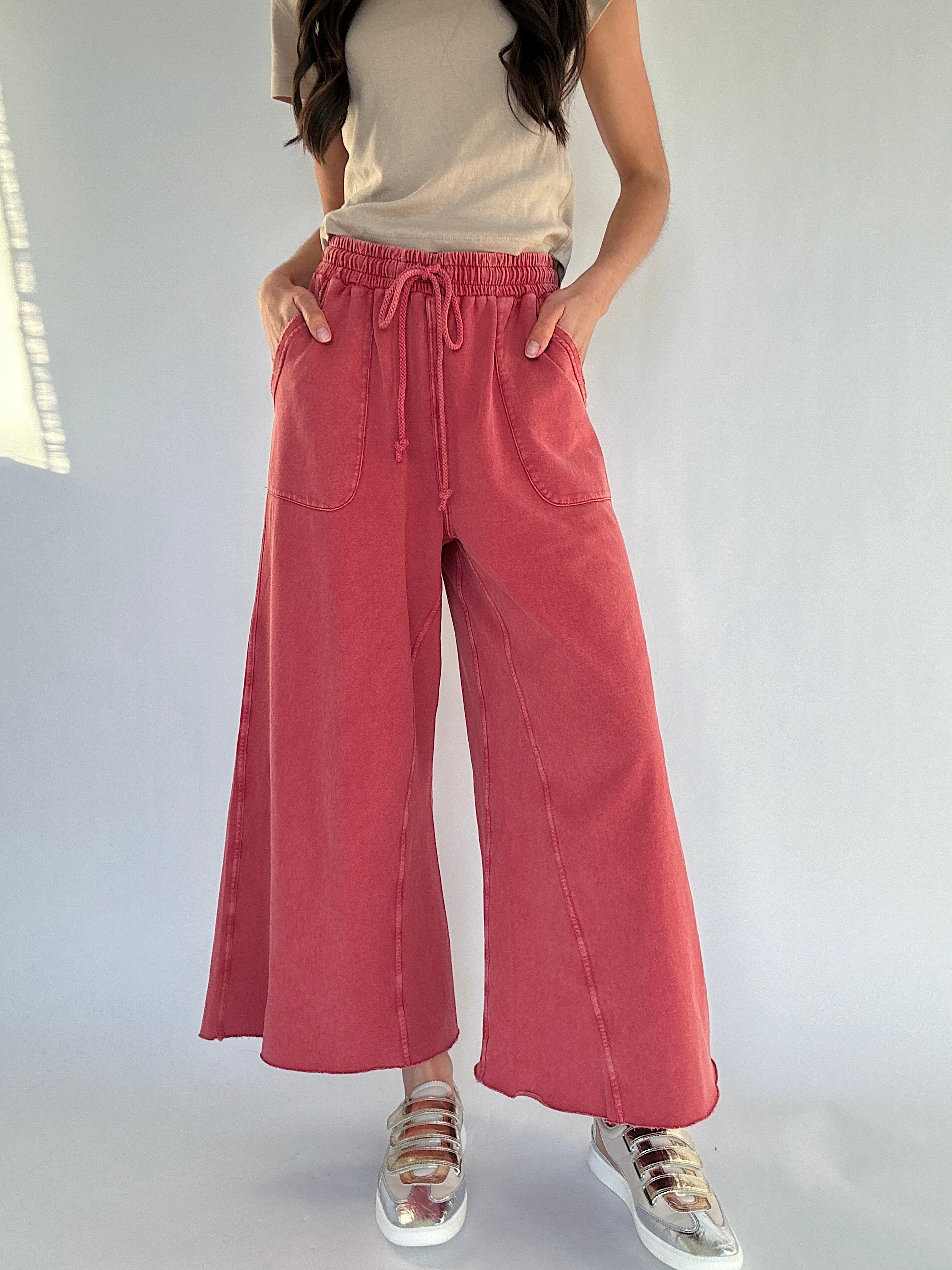 Person wearing red wide-leg sweatpants and a beige top on a plain background with metallic sneakers