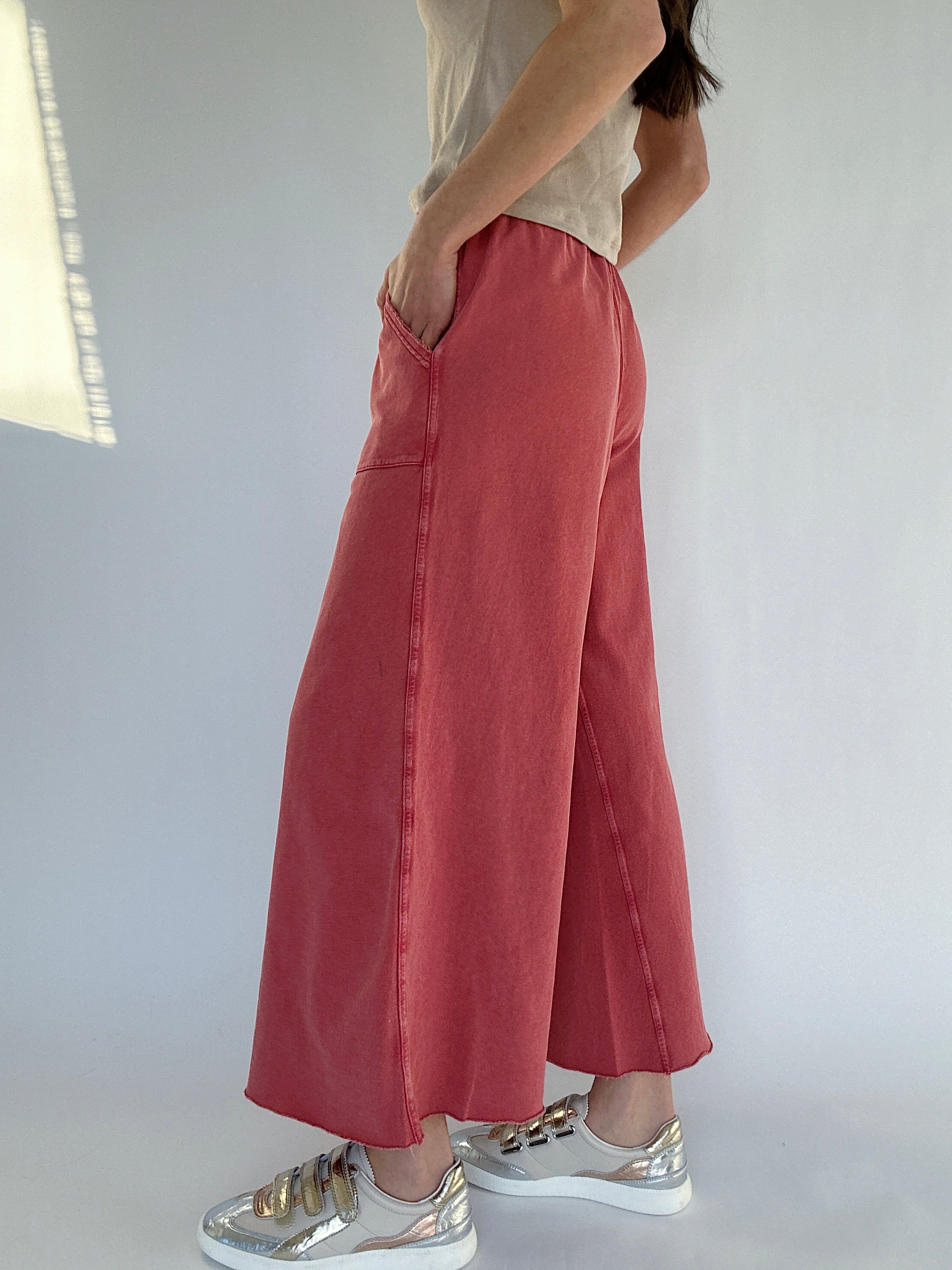 Person wearing red wide-leg sweatpants and silver sneakers on a plain background showing side pockets