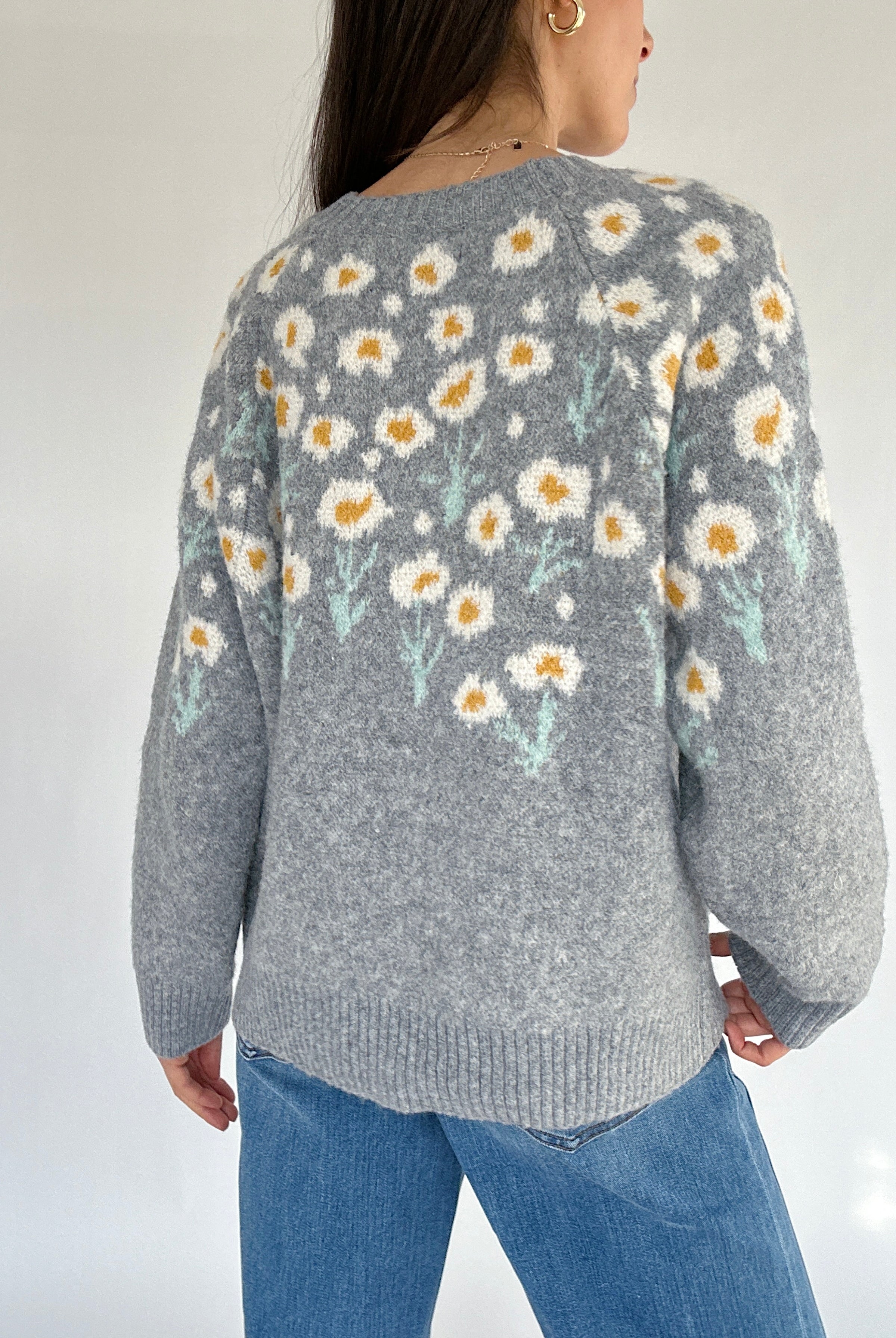 Person wearing a gray sweater with floral pattern on a plain background from the back